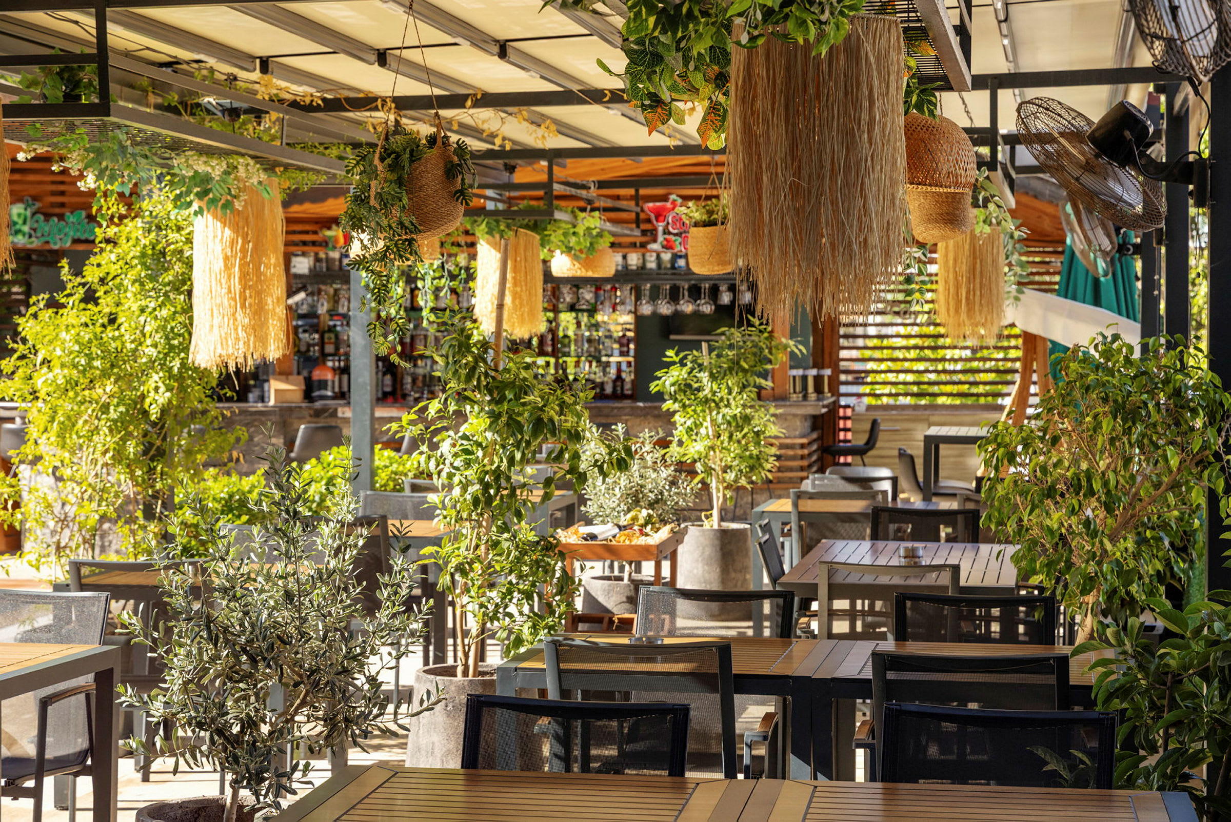 En utendørs restaurant dekket av planter og dekorasjoner med trebord og stoler. (AI-generert tekst)