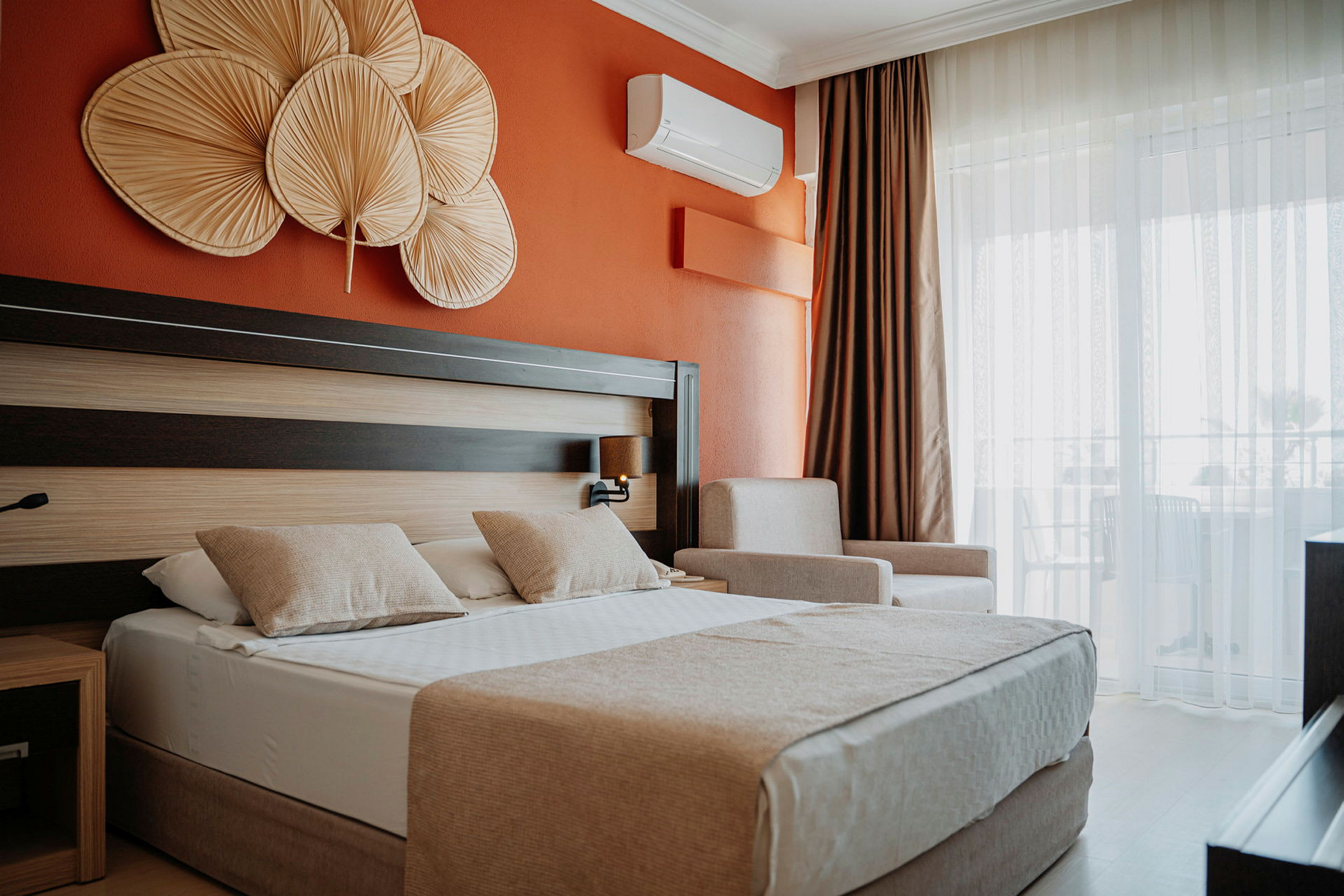 Hotellrom med oransje vegg, dobbeltseng med to puter og dekorative gjenstander over sengen. (AI-generert tekst)