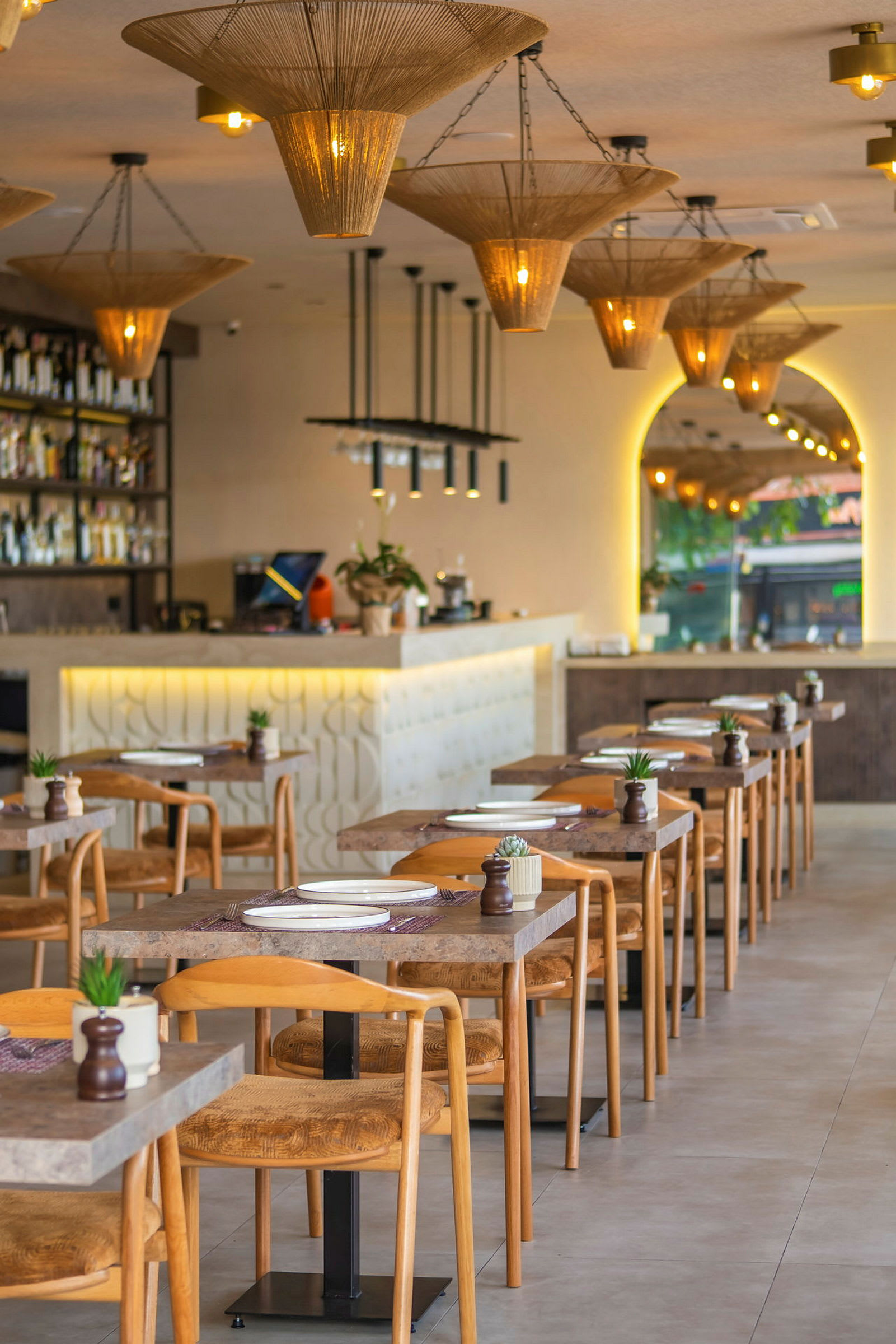 Bilde av en moderne restaurant med oppsatte bord og stoler, samt dekorative taklamper. (AI-generert tekst)