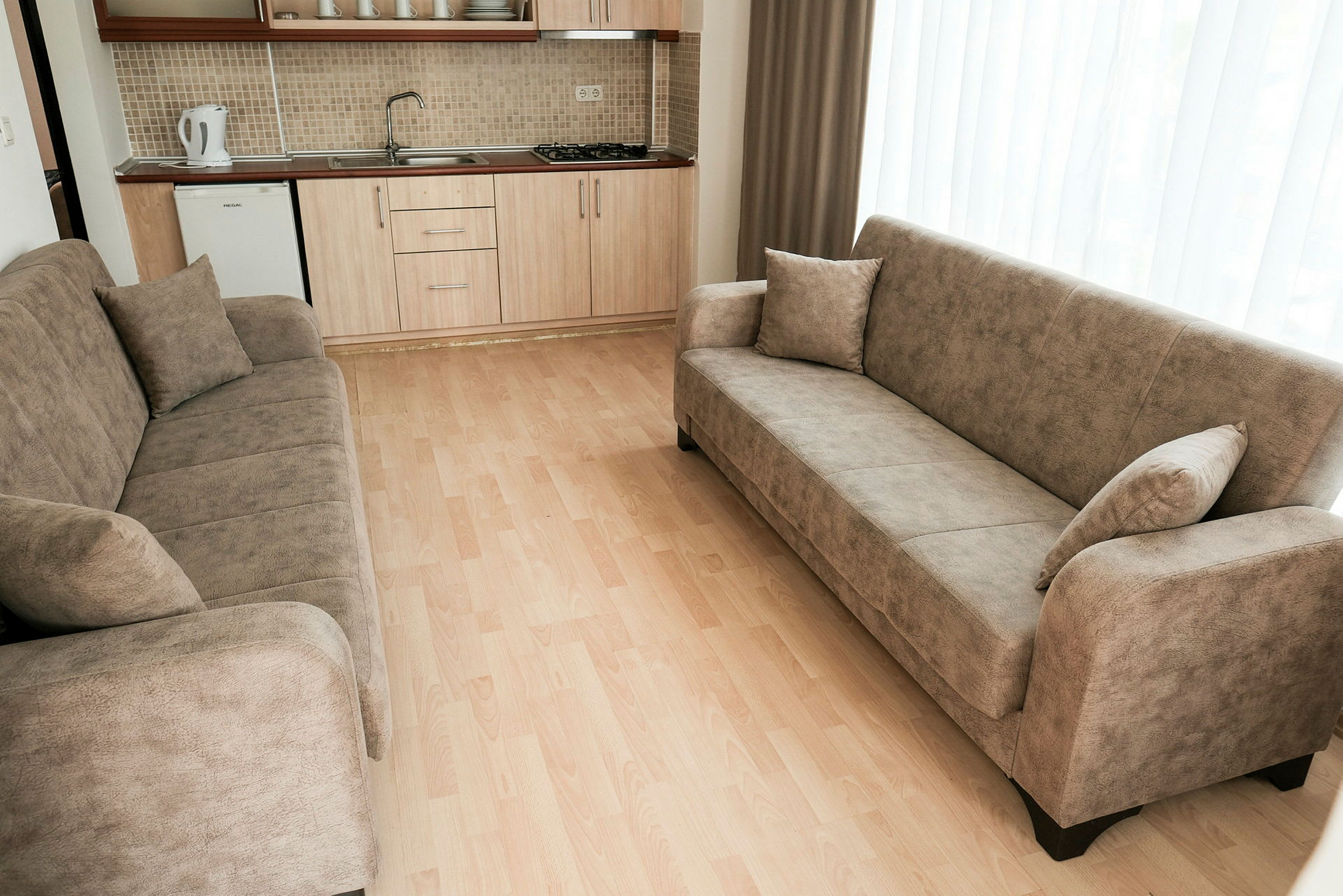 En stue med to beige sofaer og et kjøkken i bakgrunnen. (AI-generert tekst)