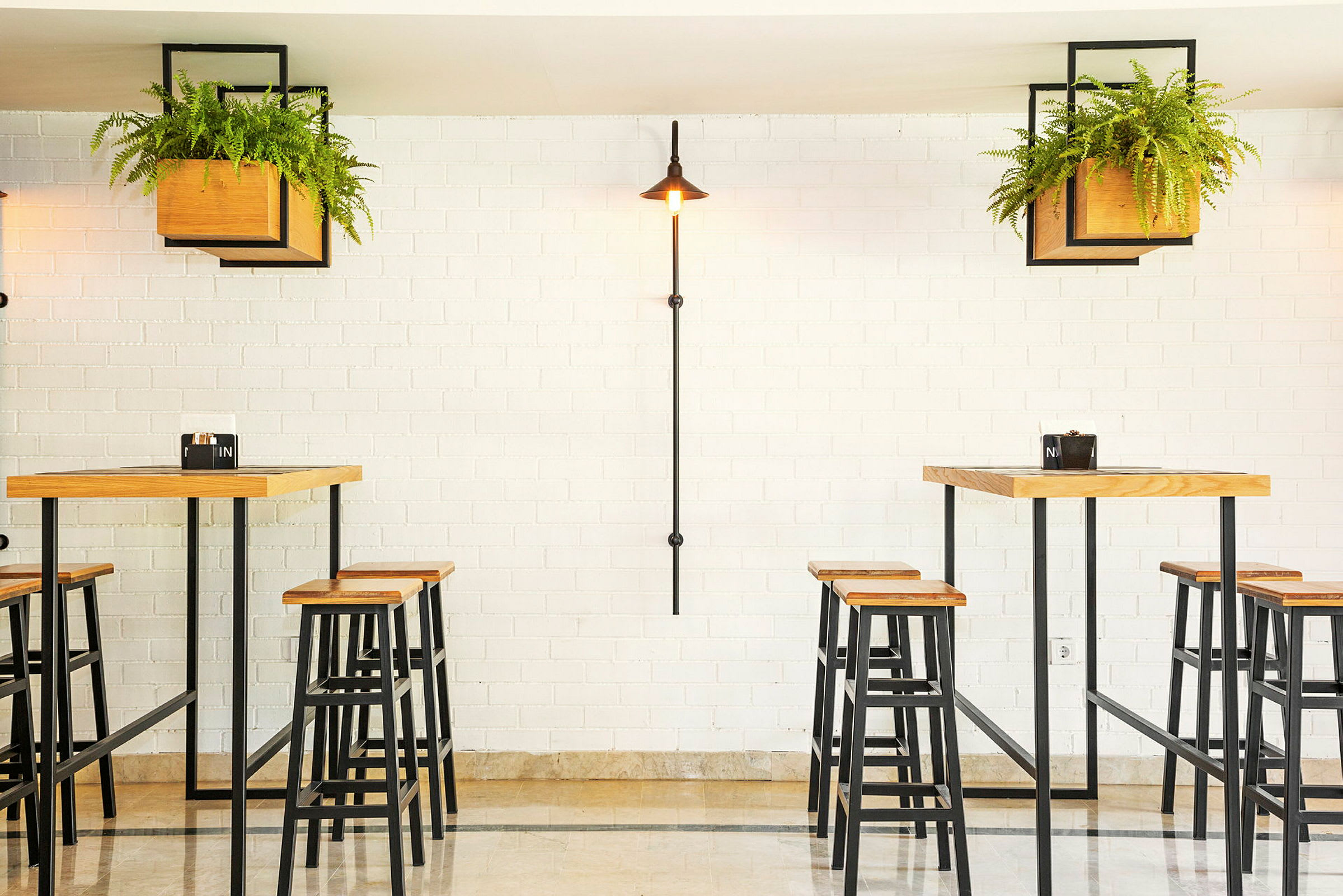 En lys restaurant med høye bord og stoler, omgitt av grønne planter. (AI-generert tekst)