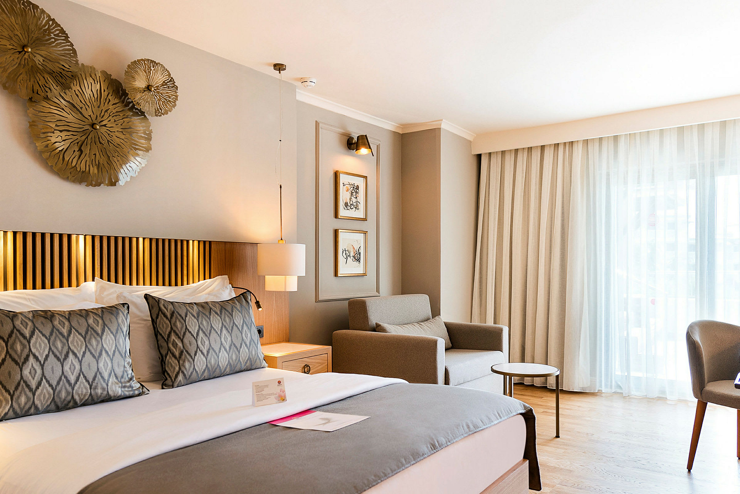 Et hotellrom med en stor seng, en lenestol og et bord ved et vindu. (AI-generert tekst)