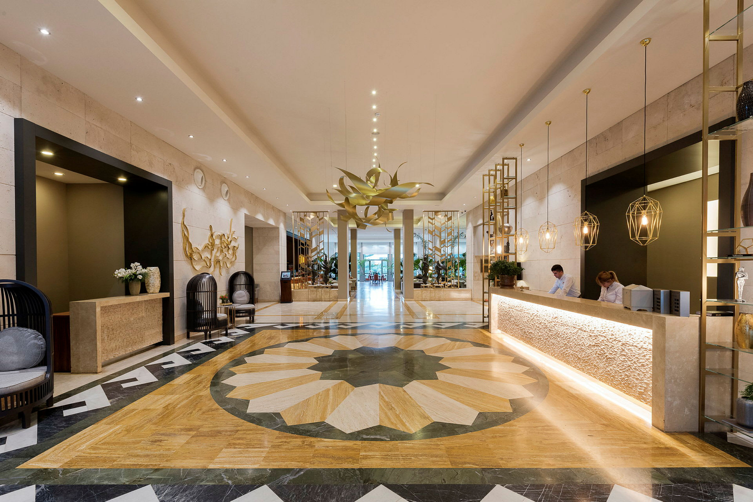 En elegant hotellobby med marmorgulv, en resepsjon med ansatte, moderne dekorasjoner og en stor blomsterlignende lysekrone. (AI-generert tekst)
