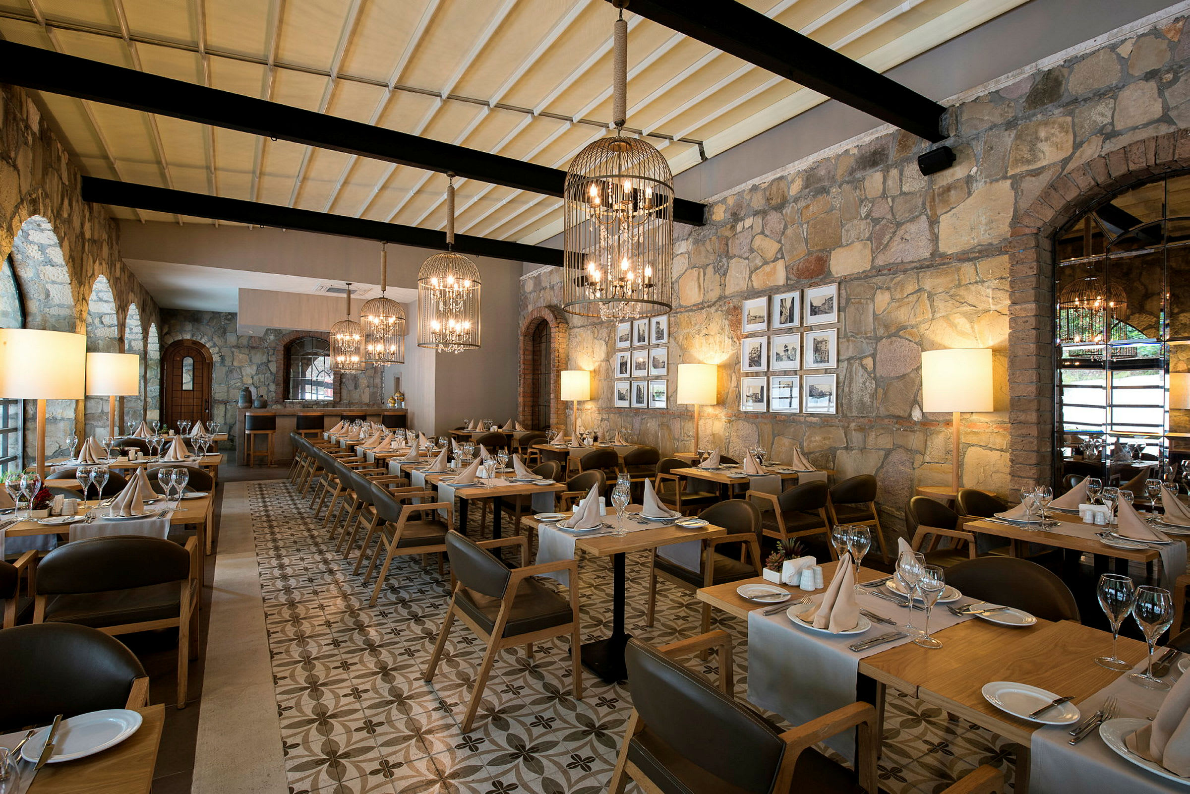 En restaurant med oppsatte bord og stoler, steinvegger og taklamper. (AI-generert tekst)