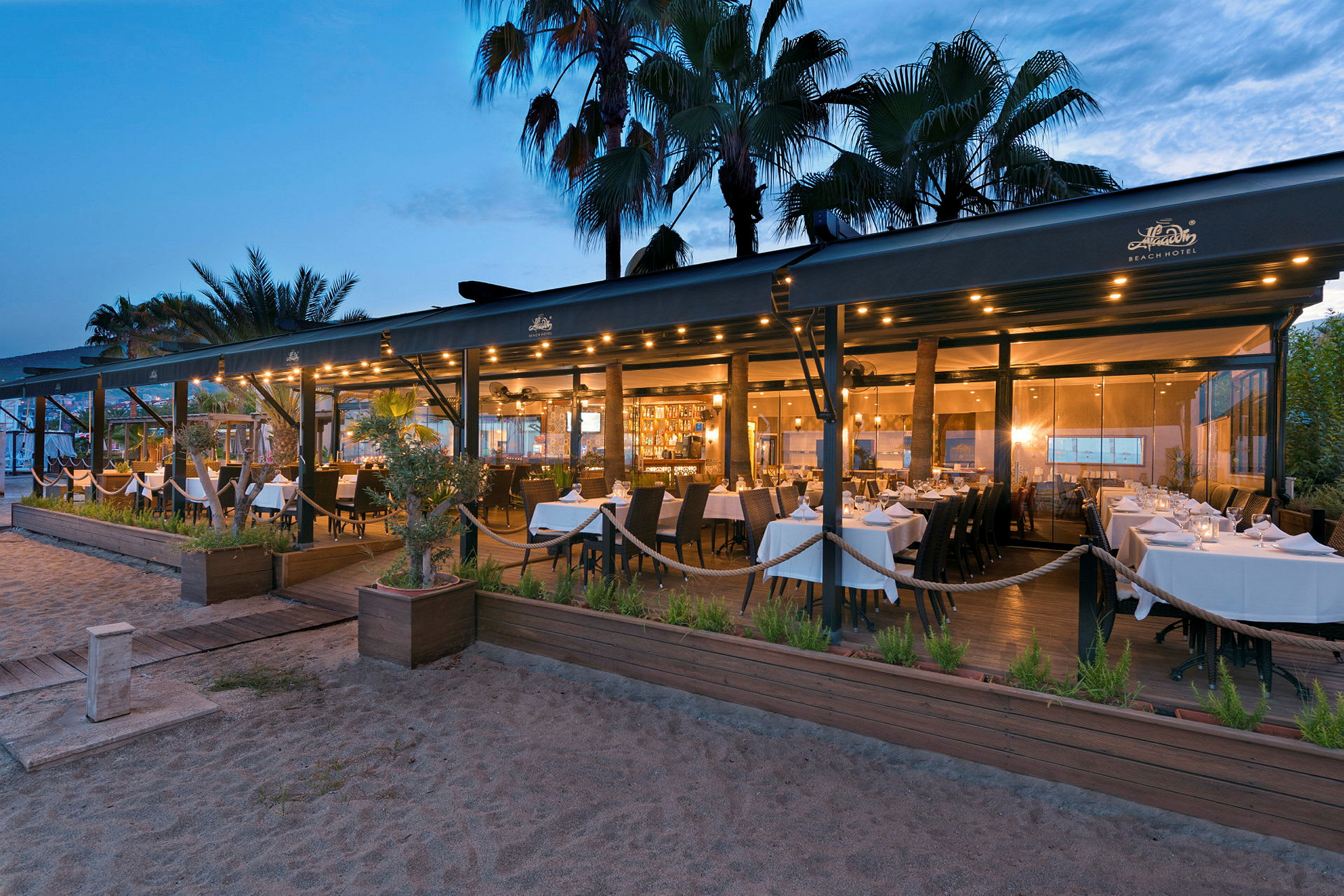 En restaurant ved stranden med hvite duker på kveldstid. (AI-generert tekst)