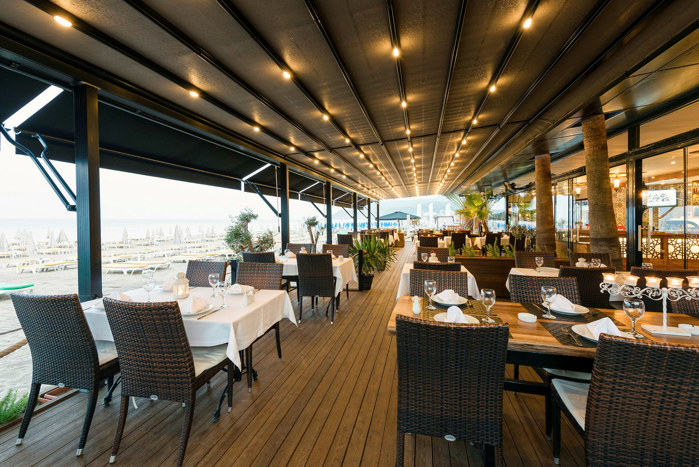 En utendørs restaurant med dekkede bord og stoler nær stranden. (AI-generert tekst)