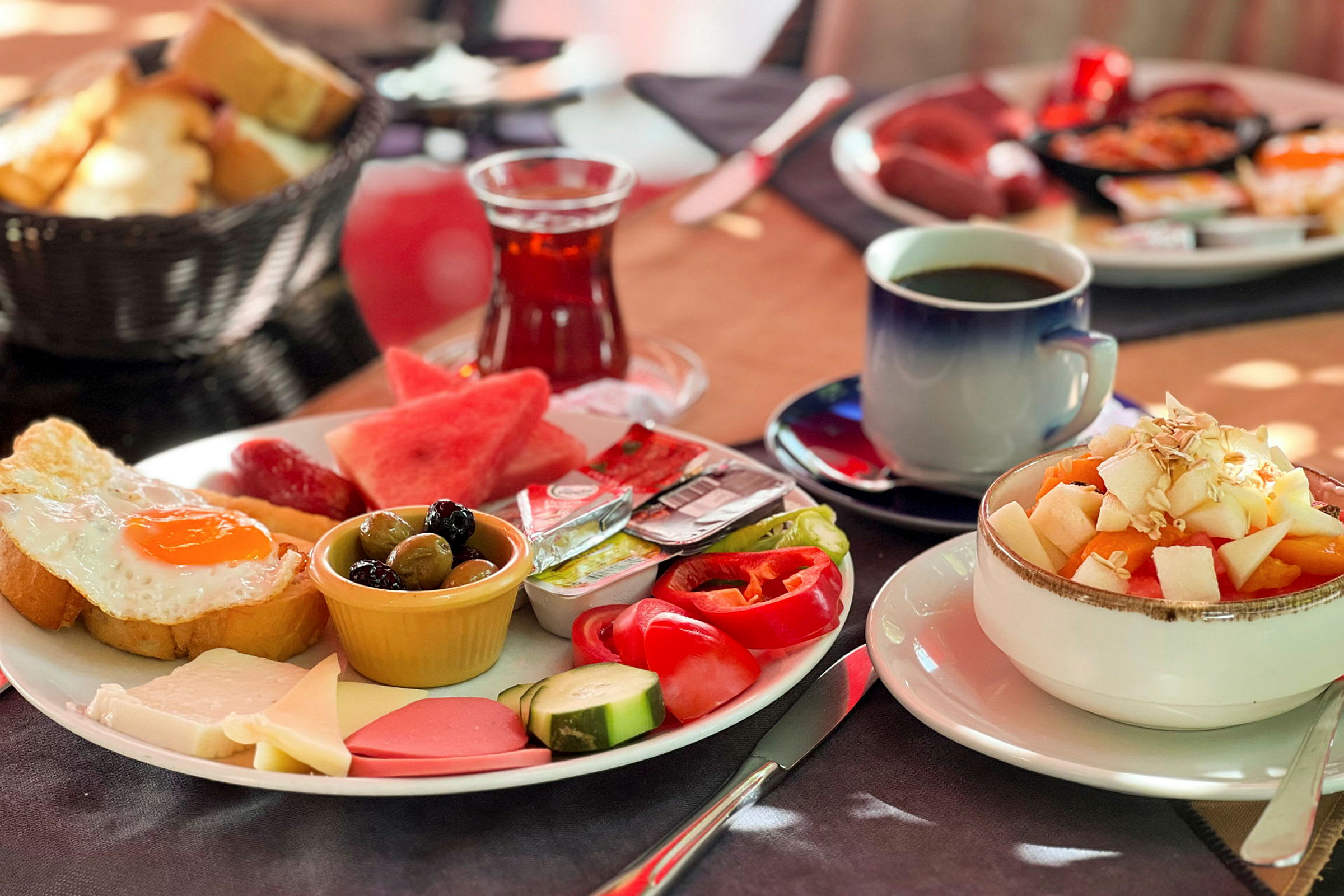 En tallerken med frokostmat inkludert stekt egg, grønnsaker, ost og andre tilbehør, ved siden av en bolle med fruktsalat og drikke. (AI-generert tekst)