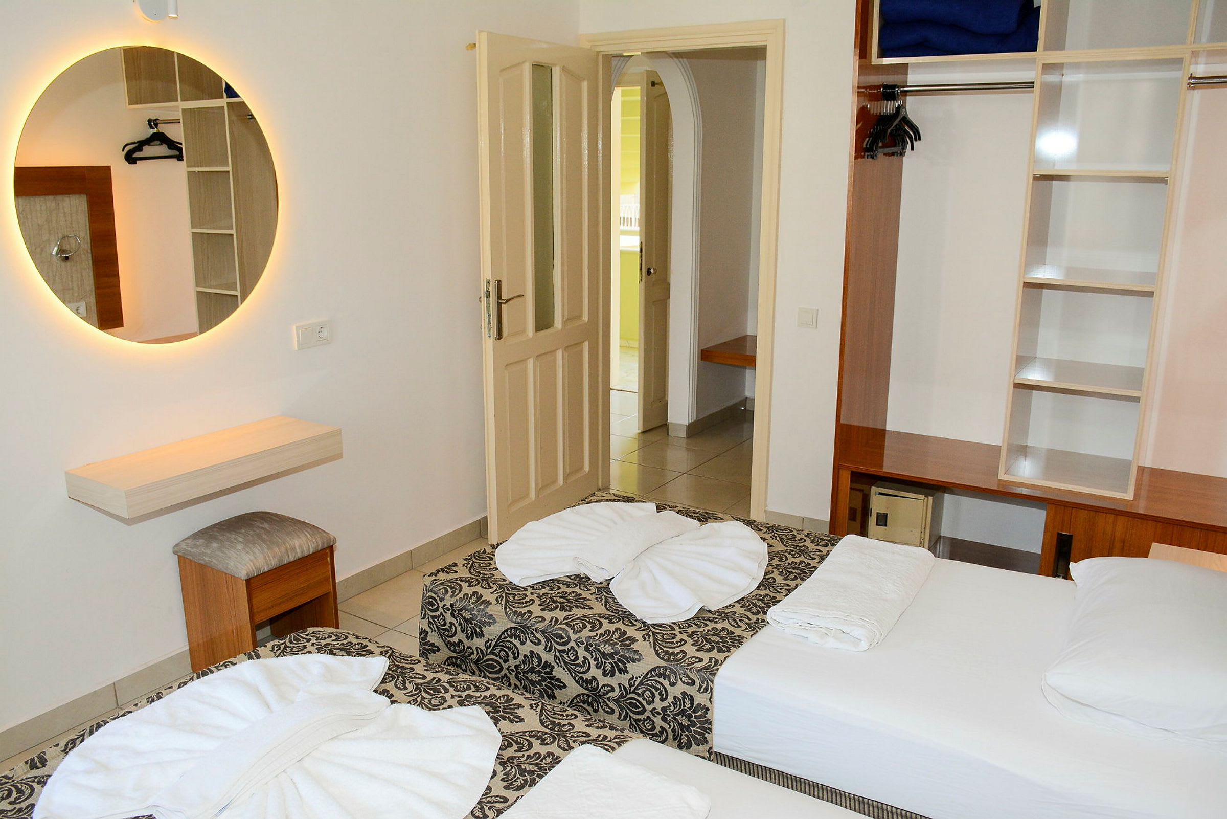 Et hotellrom med to enkeltsenger, en garderobe og et rundt speil på veggen. (AI-generert tekst)