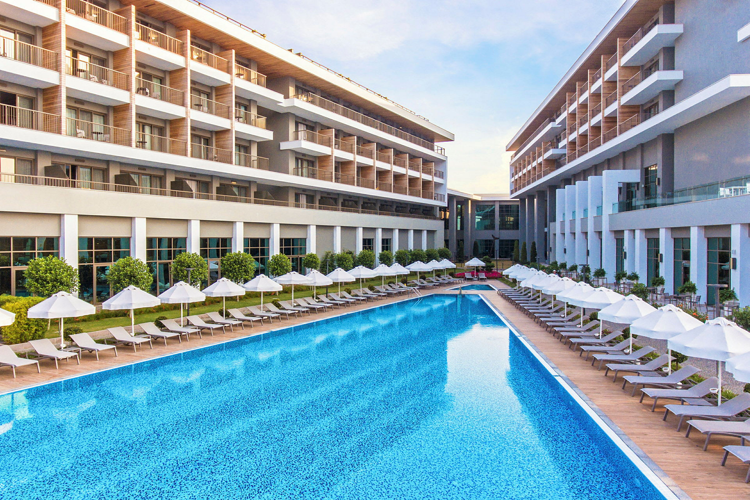 Moderne hotellbygning med stort basseng og solsenger med parasoller. (AI-generert tekst)