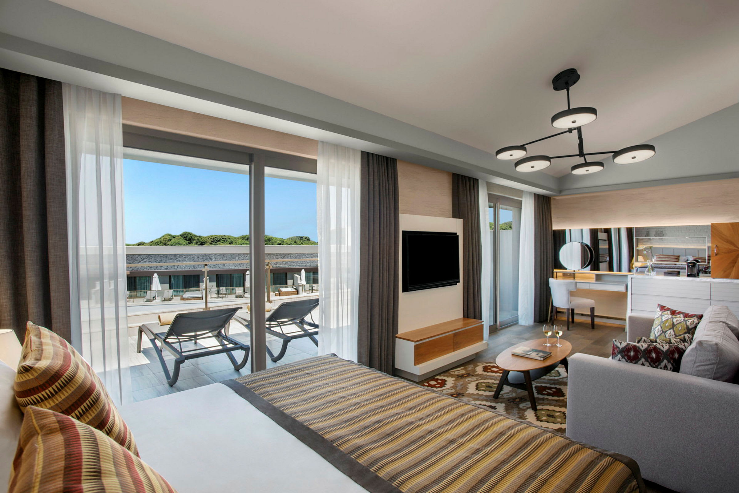 Et moderne hotellrom med en dobbeltseng, sittegruppe og utsikt over et basseng fra balkongen. (AI-generert tekst)