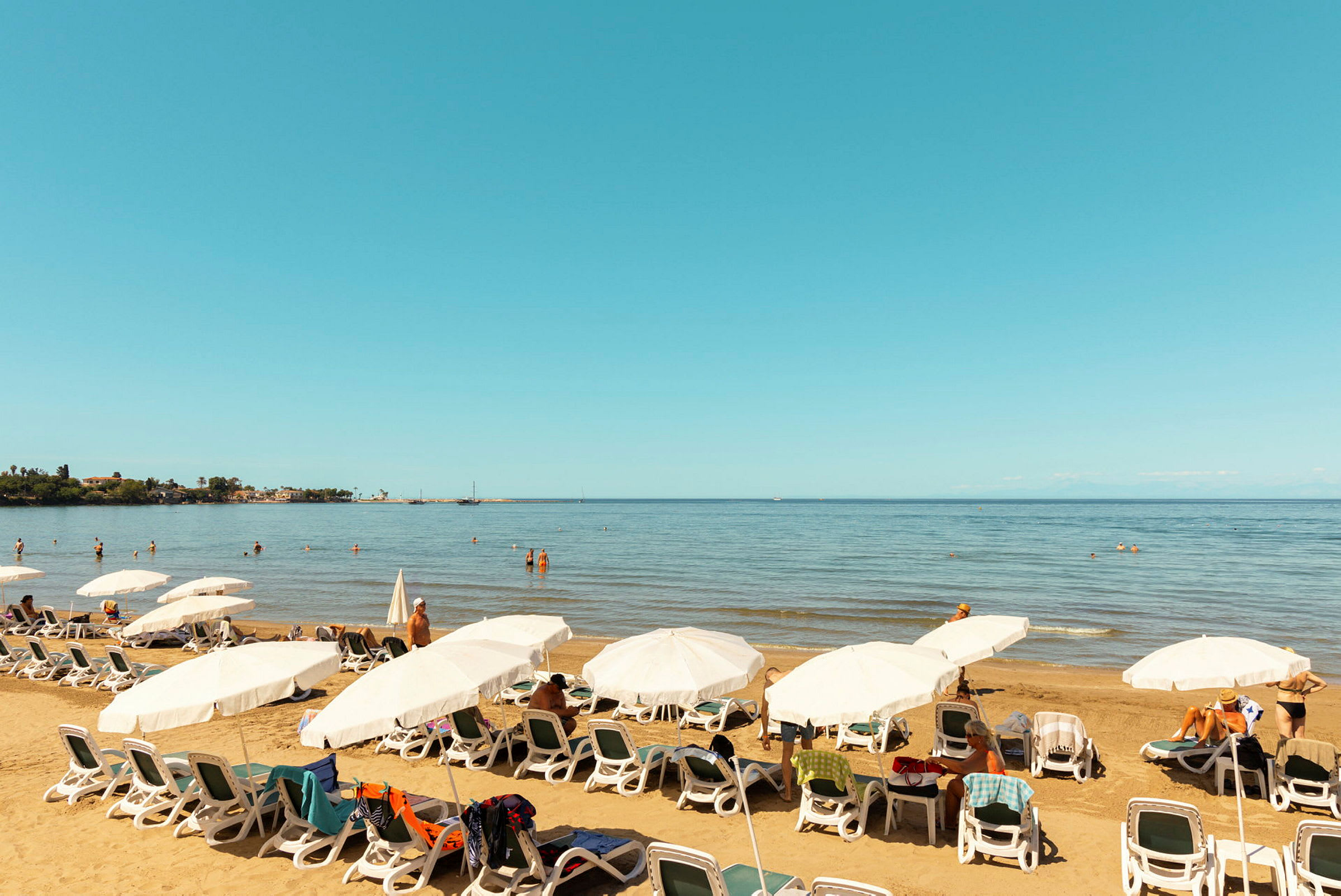 En strand med solsenger og parasoller samt folk som svømmer i havet. (AI-generert tekst)