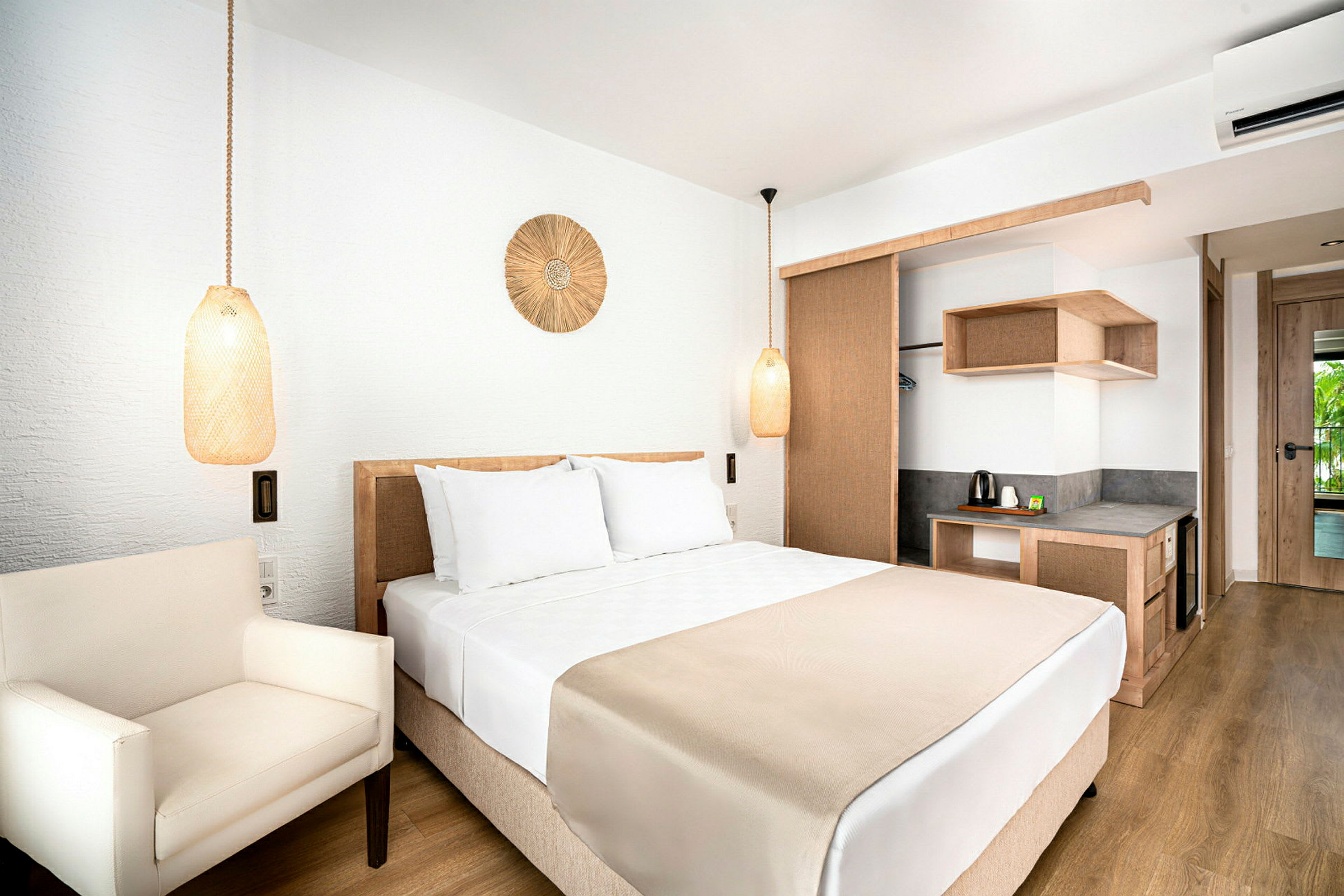 Hotellrom med en dobbeltseng, hvite sengetøy og beige detaljer. Rommet har en lenestol og en skrivekrok med vannkoker. (AI-generert tekst)