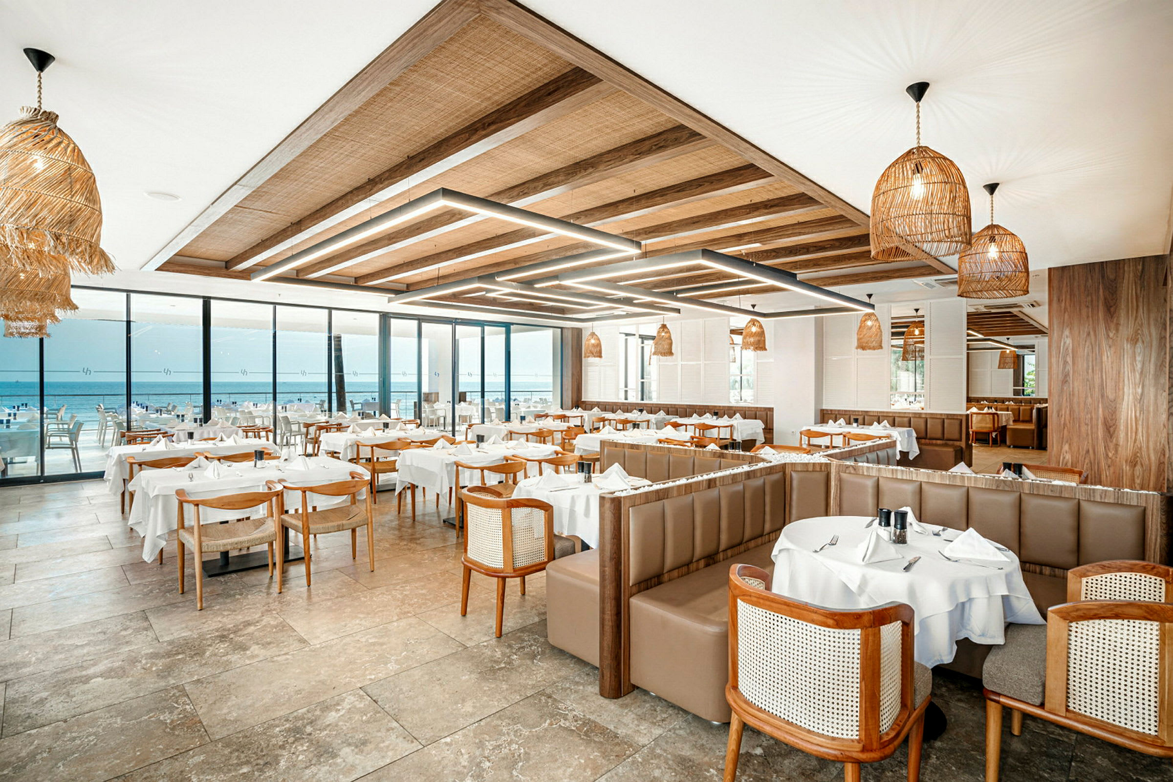 Restaurant med bord dekket med hvite duker og utsikt over havet. (AI-generert tekst)