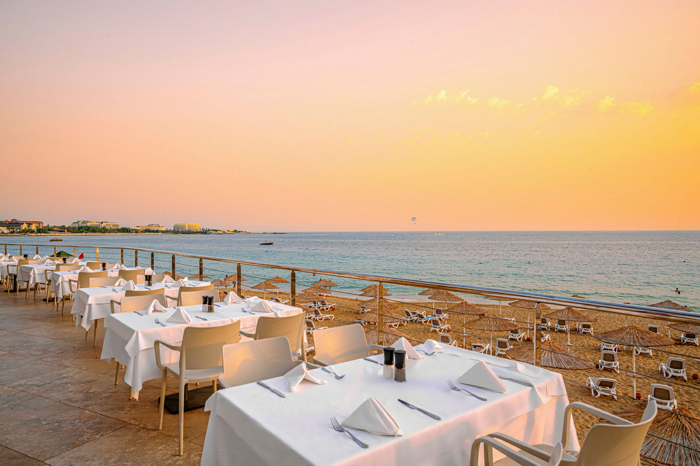 Bilde av en strand med solsenger og parasoller, samt en restaurant med dekkede bord ved havet. (AI-generert tekst)