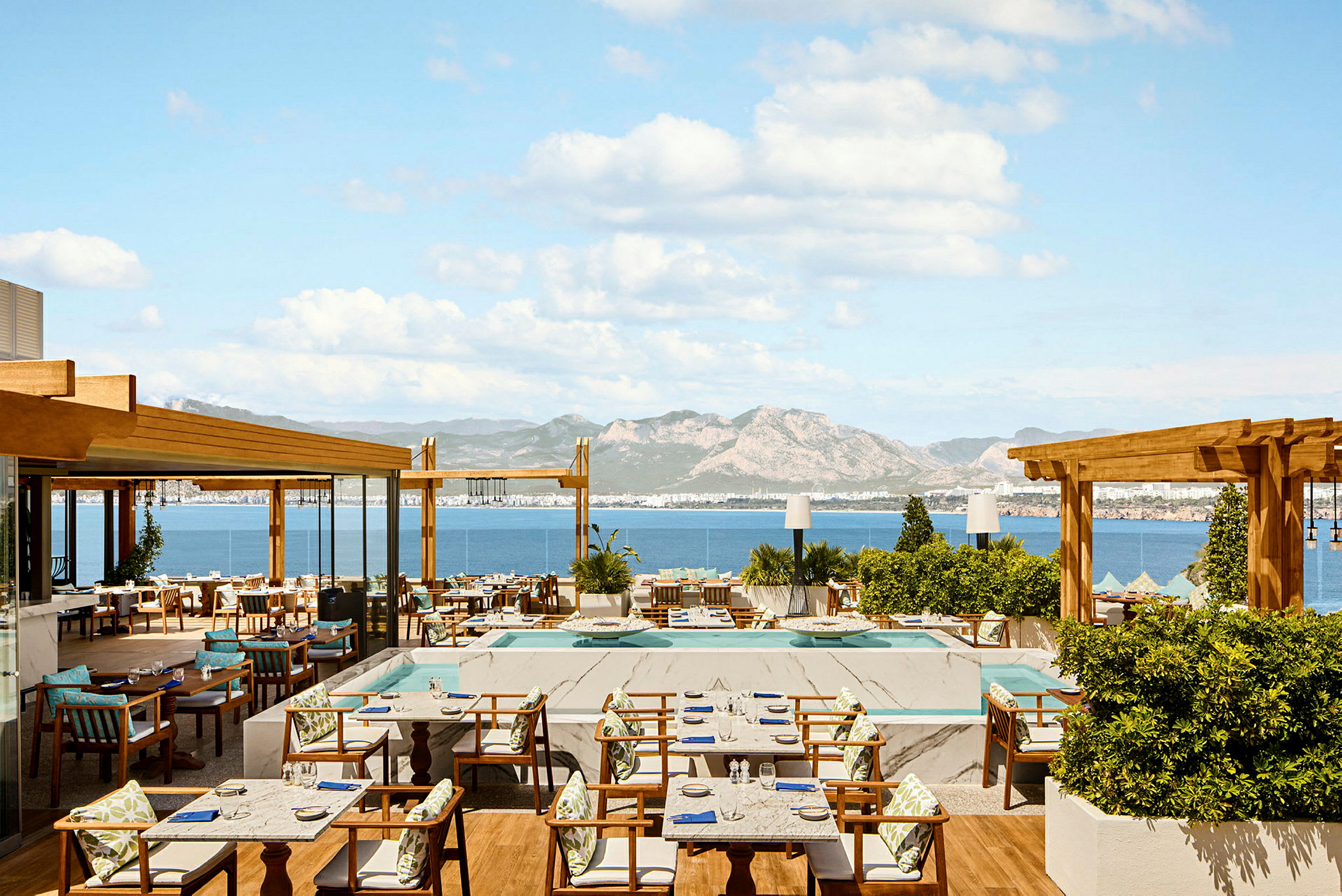 En restaurantterrasse med havutsikt og fjell i bakgrunnen. (AI-generert tekst)