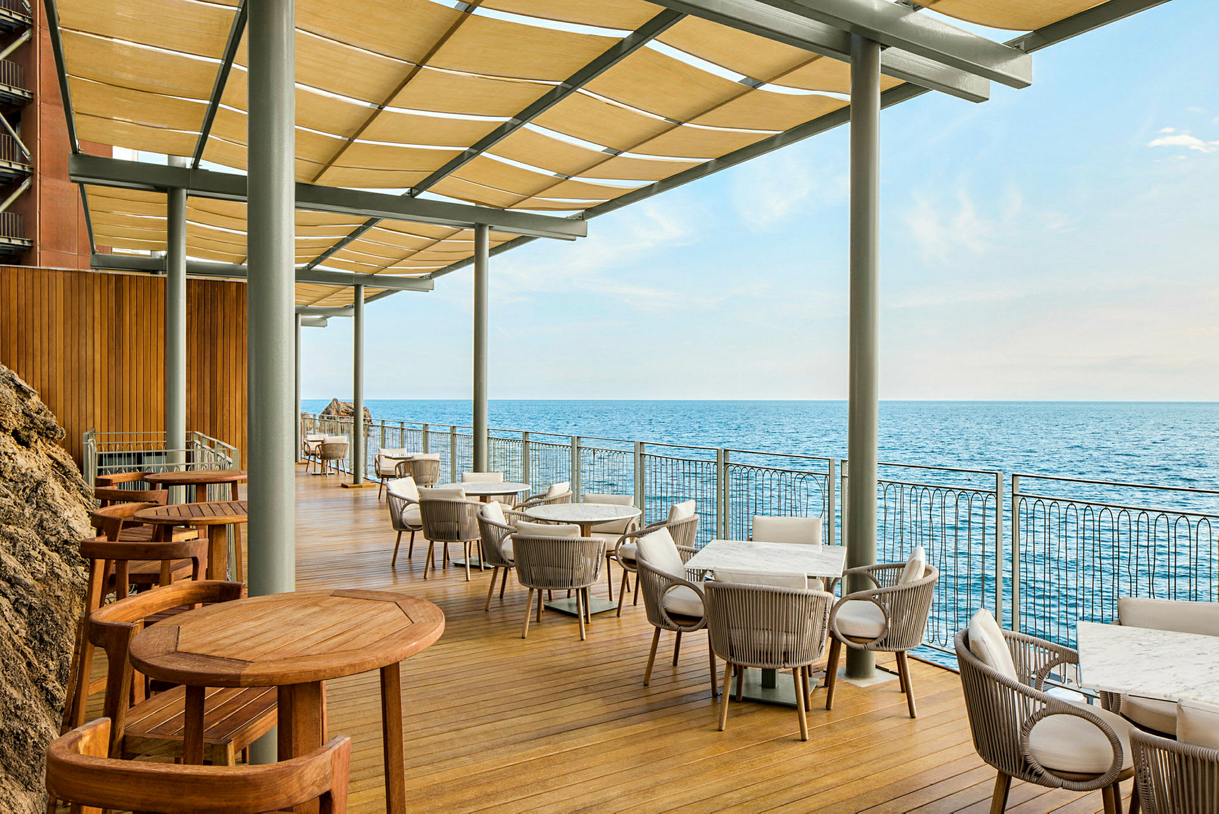 En terrasse med bord og stoler med utsikt over havet. (AI-generert tekst)