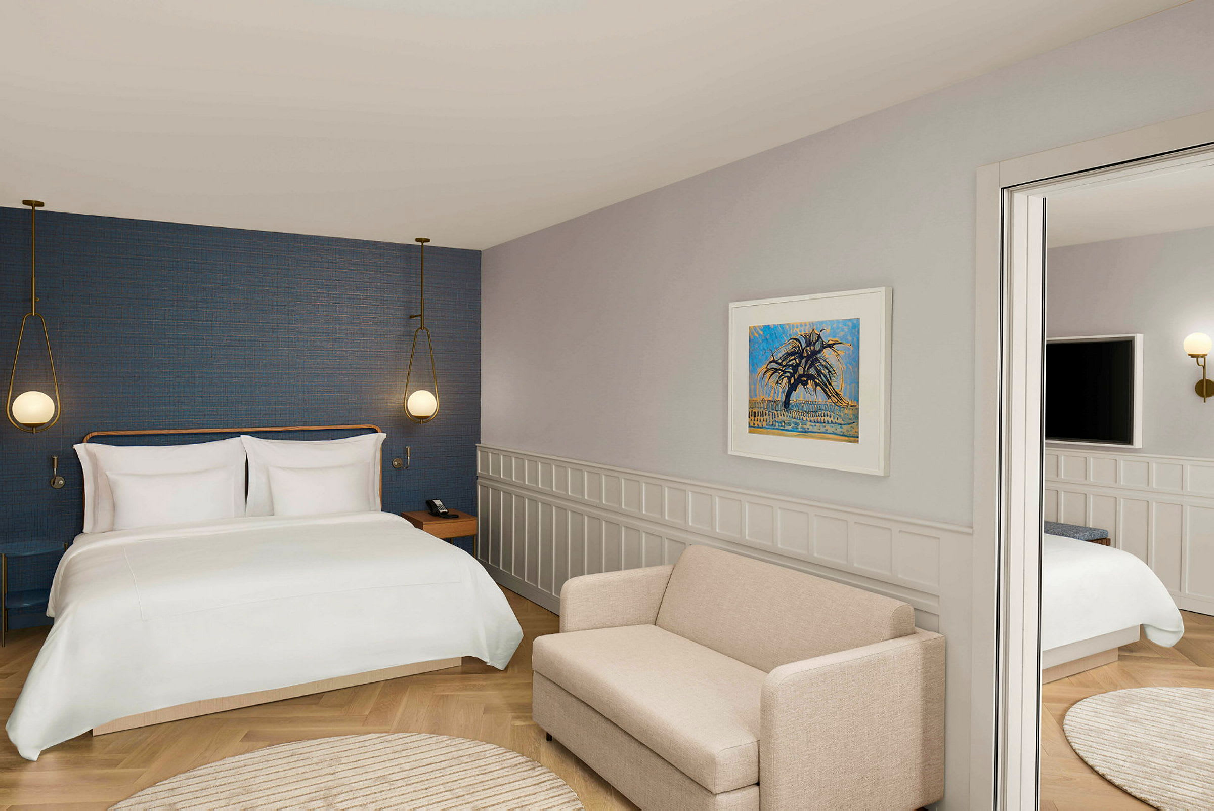 Et hotellrom med en stor seng, vegglamper, en beige sofa og kunst på veggen. (AI-generert tekst)