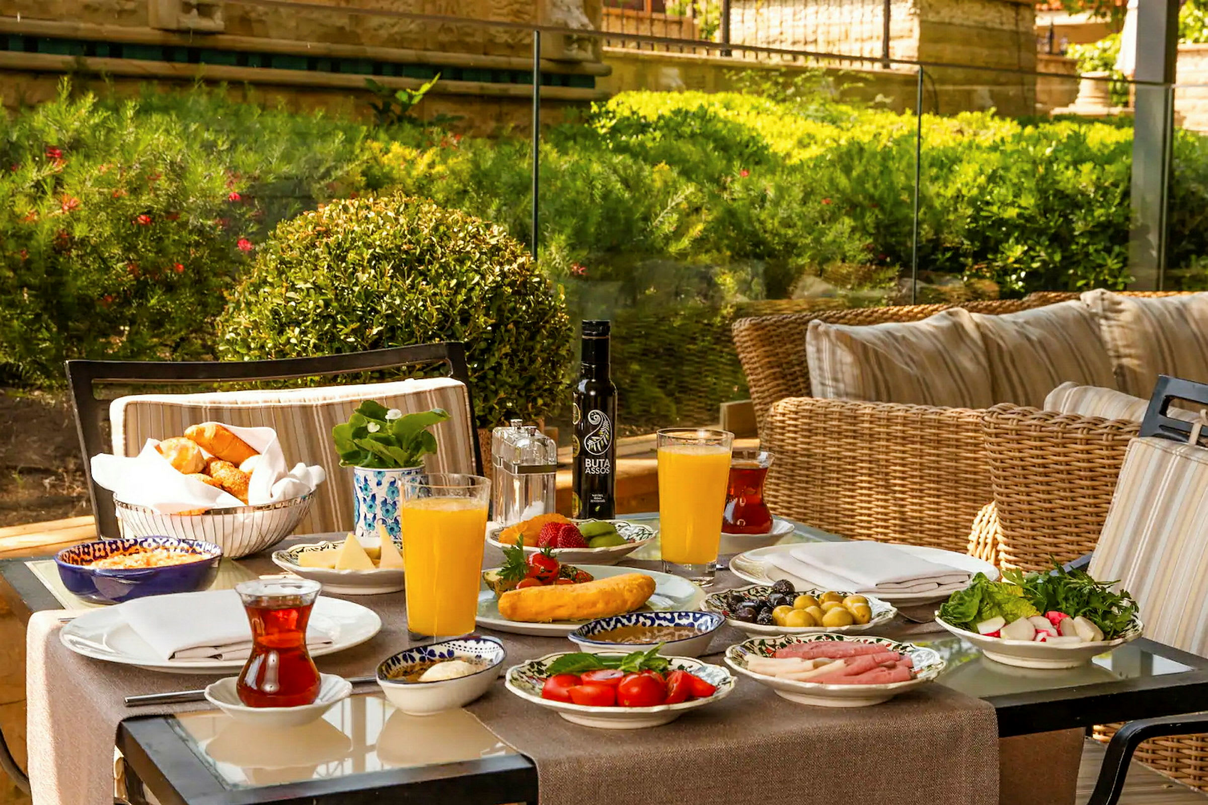 Et fargerikt frokostbord med forskjellige retter, juice og te, plassert utendørs med grøntområder i bakgrunnen. (AI-generert tekst)