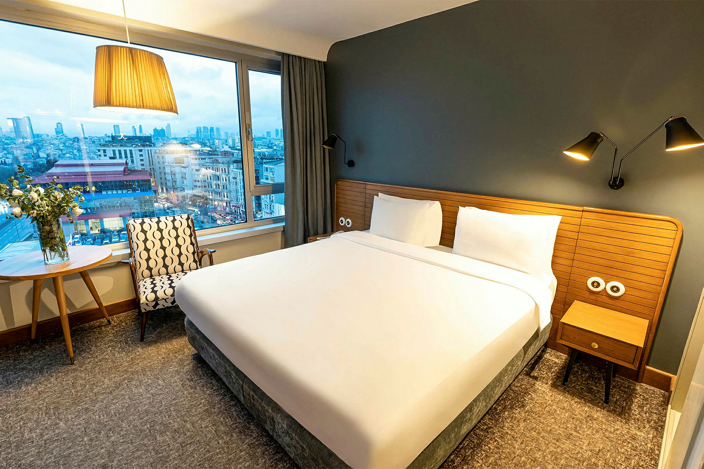 Et hotellrom med en stor seng, vindu og utsikt over en by. (AI-generert tekst)