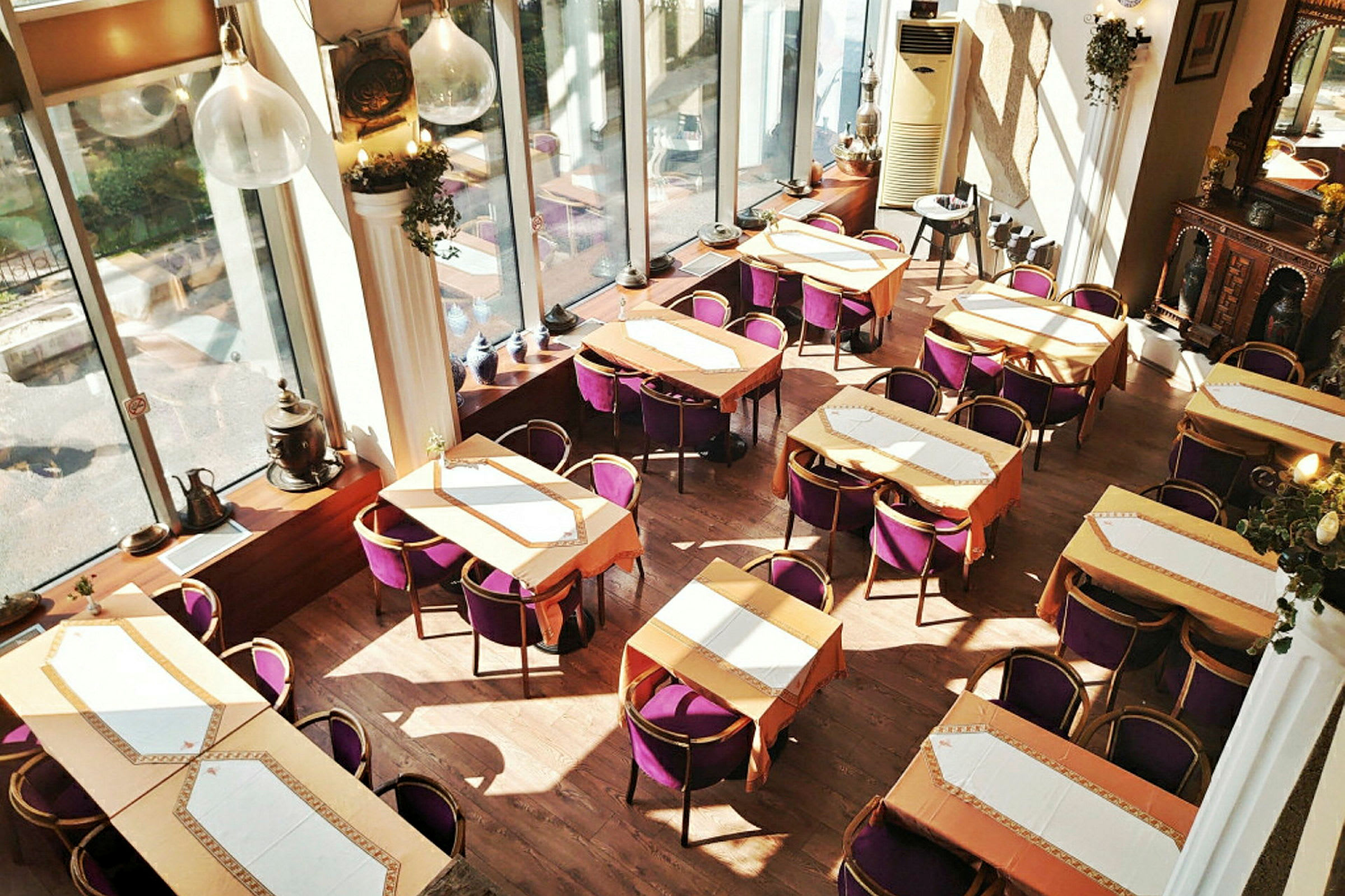 Interiør av en restaurant med flere bord og lilla stoler, store vinduer og dekorative elementer. (AI-generert tekst)