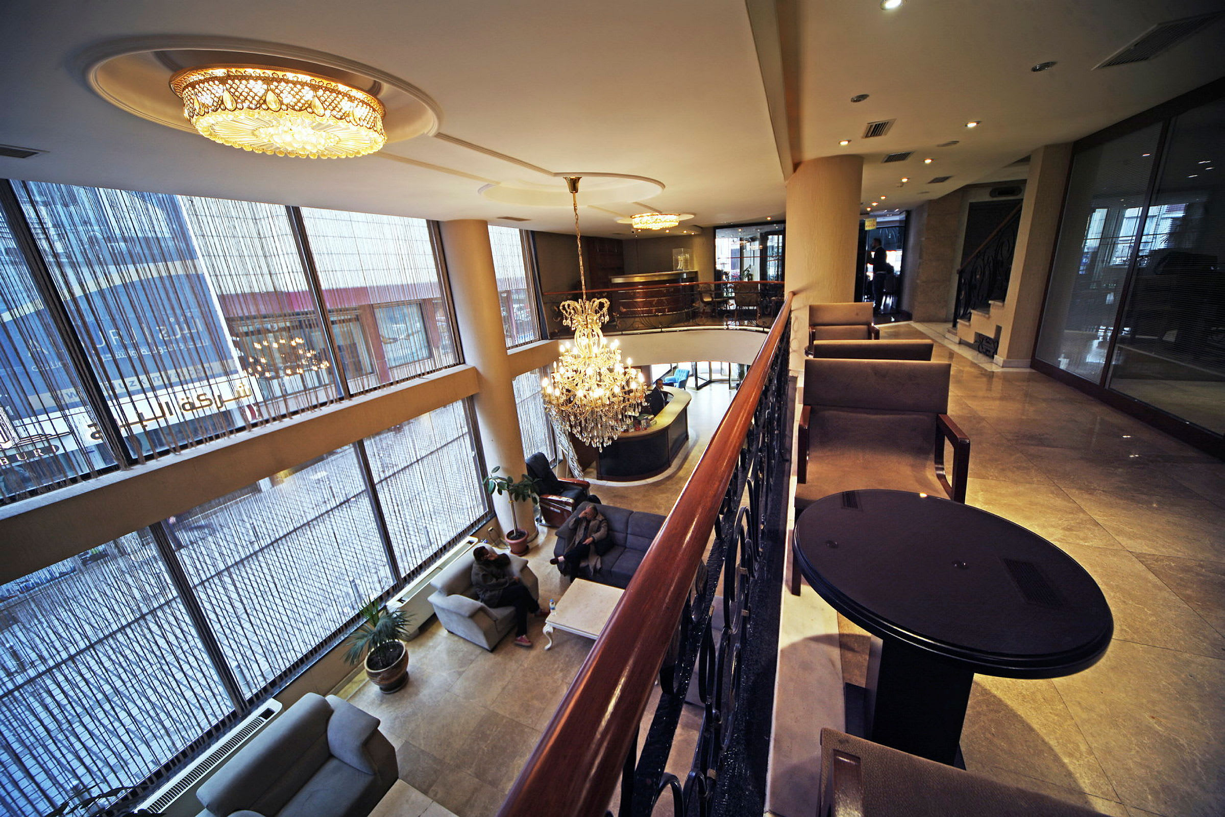 Bilde av en hotellobby med store glassvinduer, taklamper og en lysekrone. Møblerte sitteplasser finnes på ulike nivåer. (AI-generert tekst)