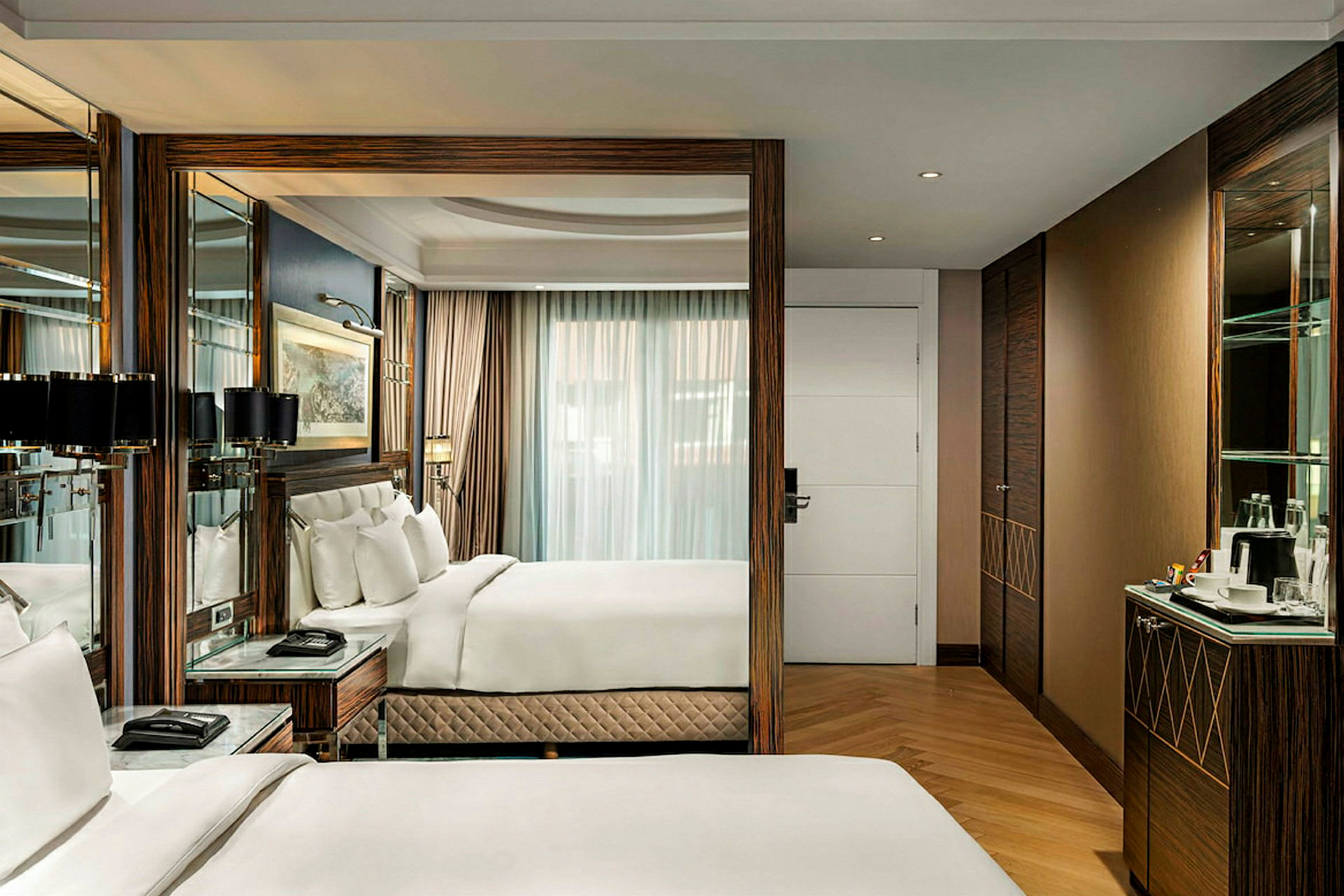 Et elegant og moderne hotellrom med komfortable senger og interiør i tre, en speilvegg og stort vindu med gardiner. (AI-generert tekst)