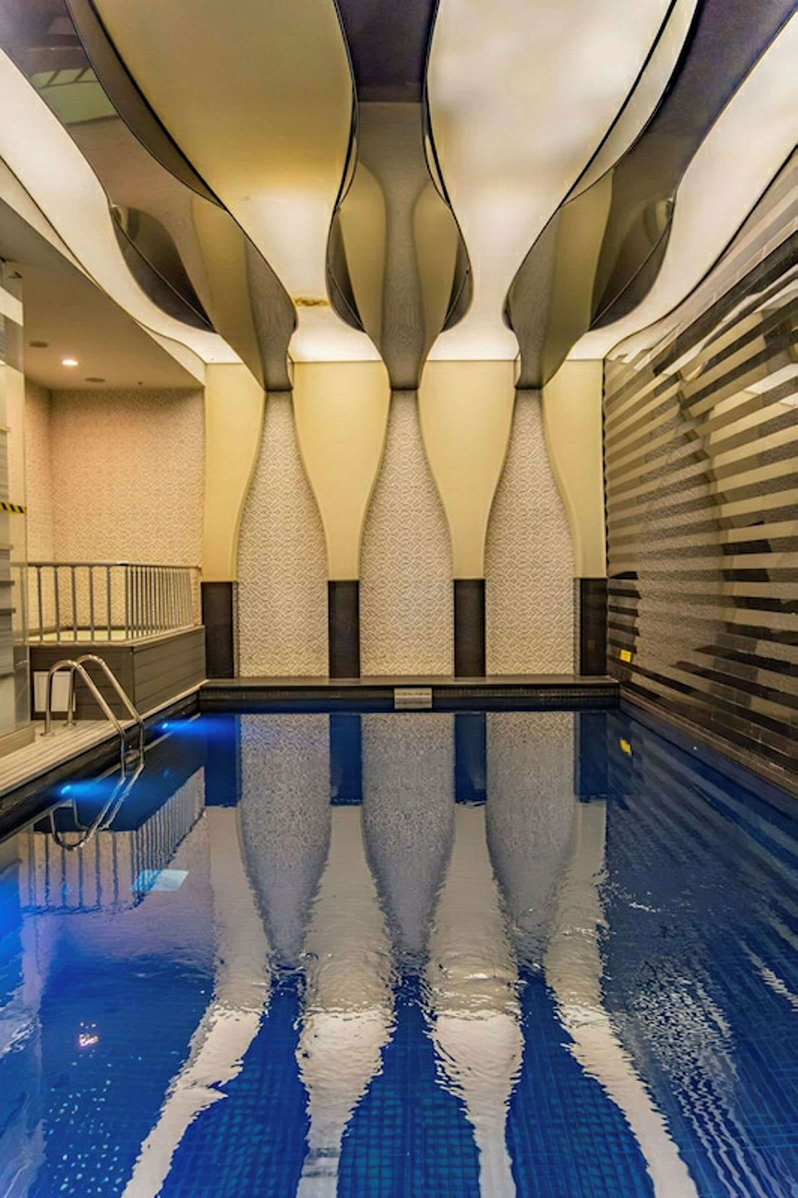 Et innendørs basseng med unikt designet tak og mønstrede vegger. Vannet speiler arkitekturen ovenfor. (AI-generert tekst)