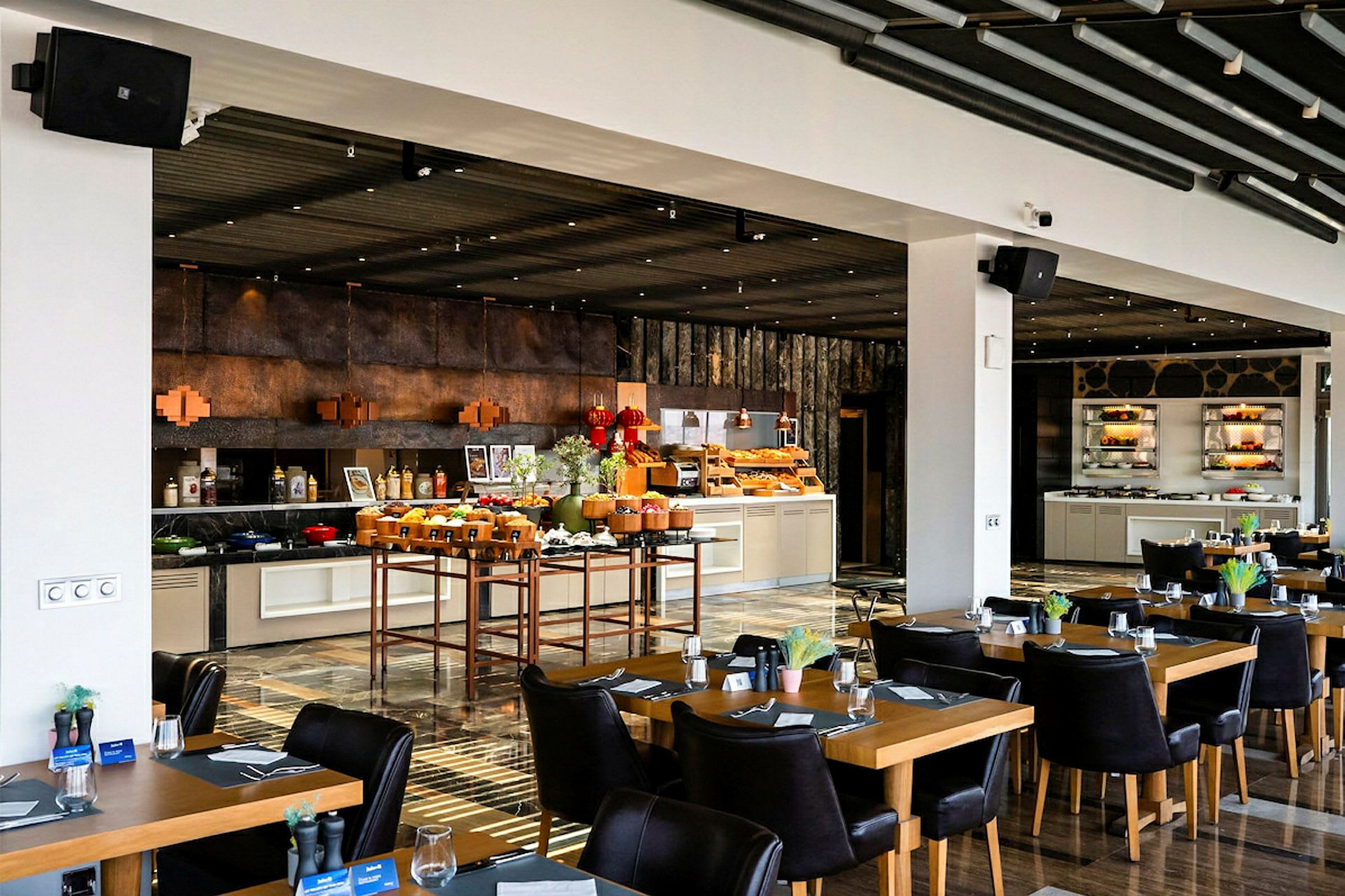 En restaurant med oppstilte bord og stoler, samt en buffédisk fylt med mat og drikke. (AI-generert tekst)