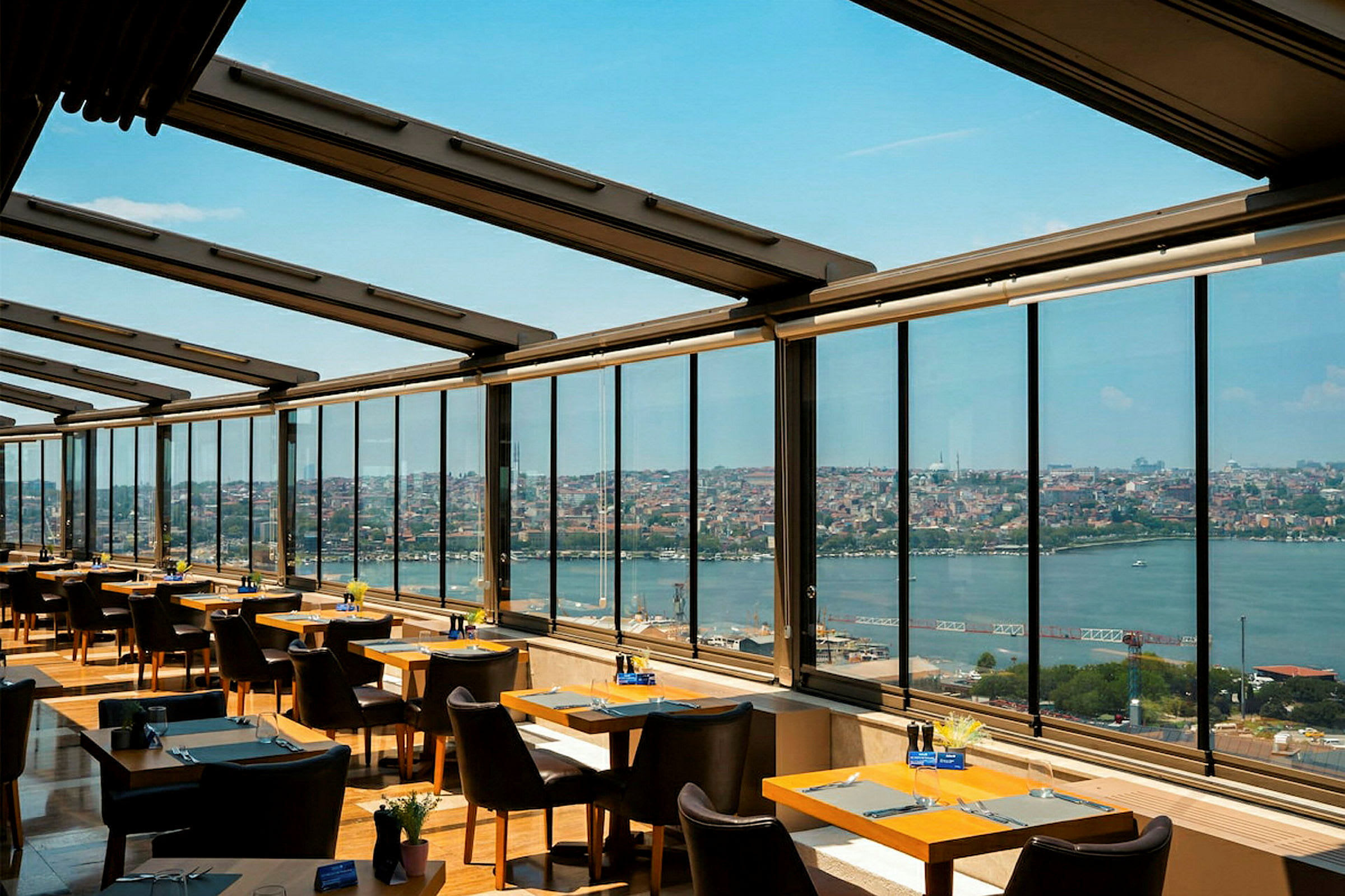 En restaurant med store vinduer som gir utsikt mot en by og et vannområde. (AI-generert tekst)