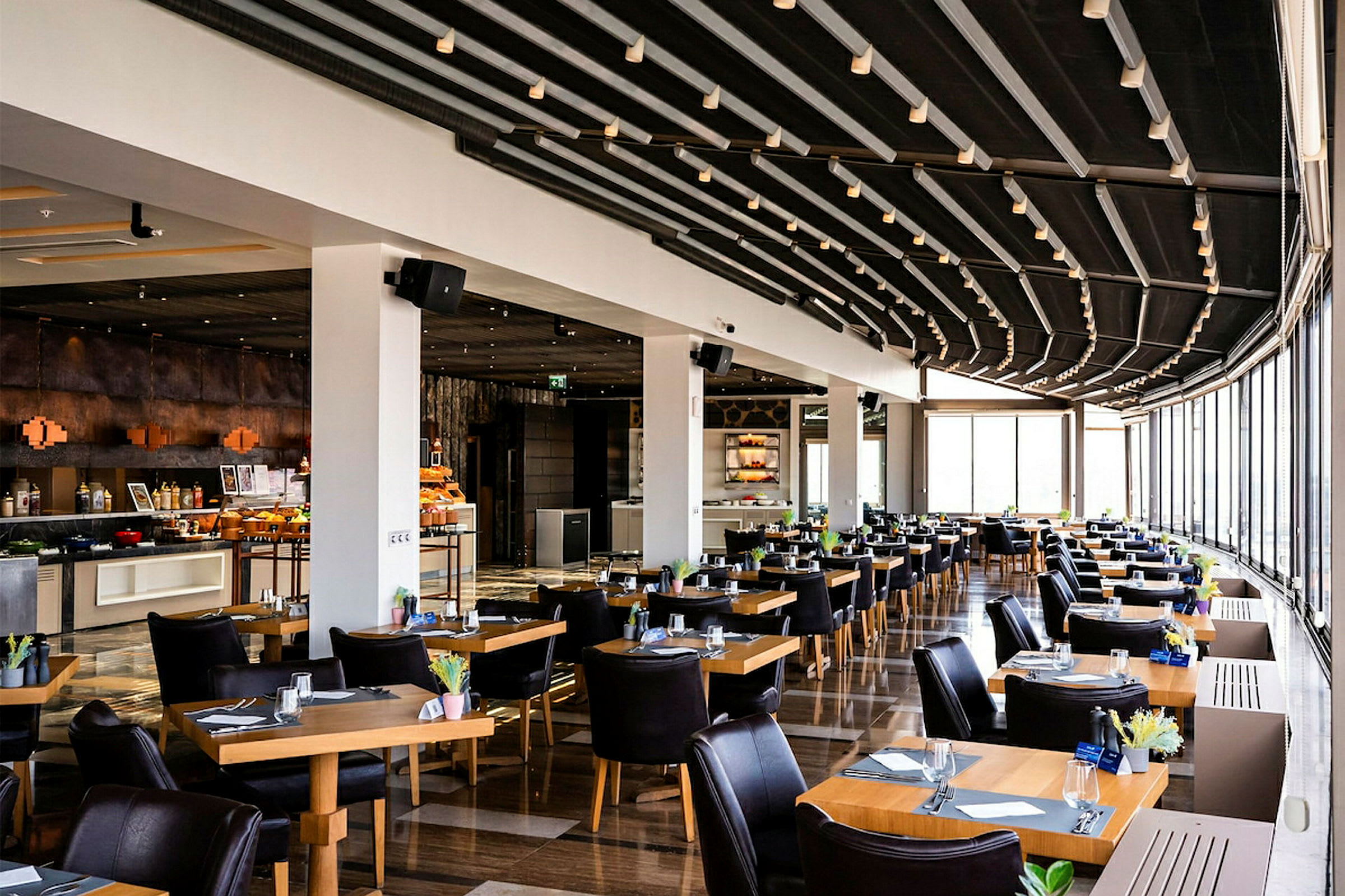 Restaurant med moderne innredede bord og stoler, stor glassflate som slipper inn lys. (AI-generert tekst)