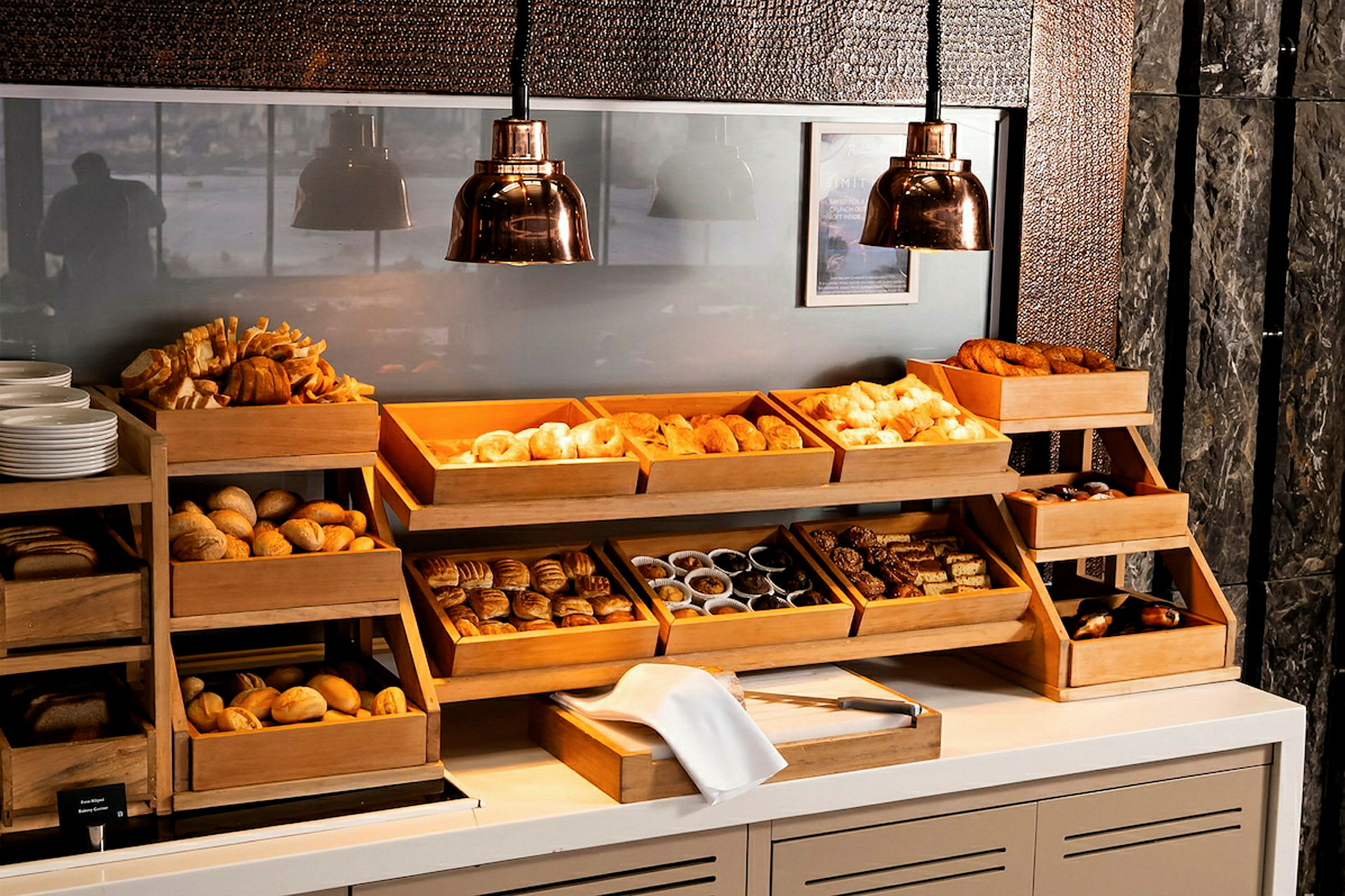 Et utvalg av brød og bakverk i trehyller på en buffet. Flere kopper og tallerkener er synlige ved siden av. (AI-generert tekst)