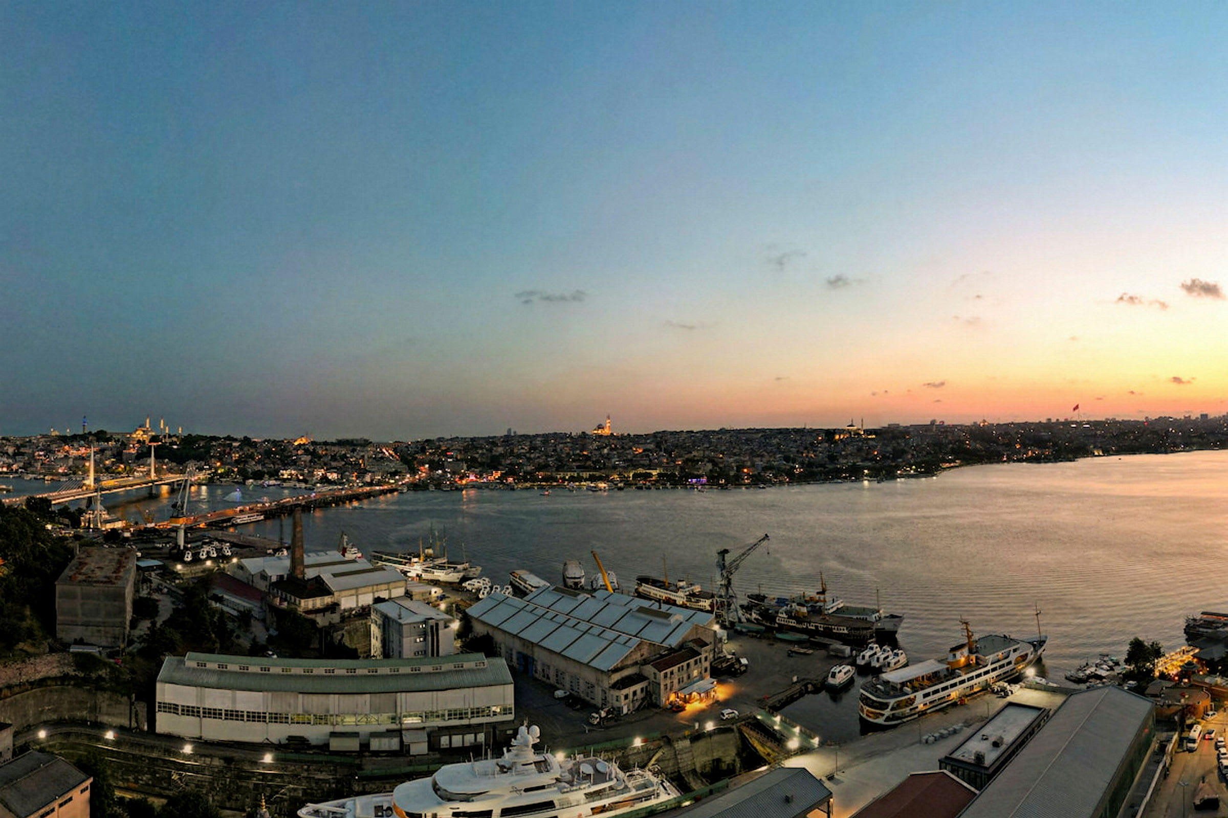 Utsikt over en havn med båter og by i bakgrunnen under solnedgang. (AI-generert tekst)