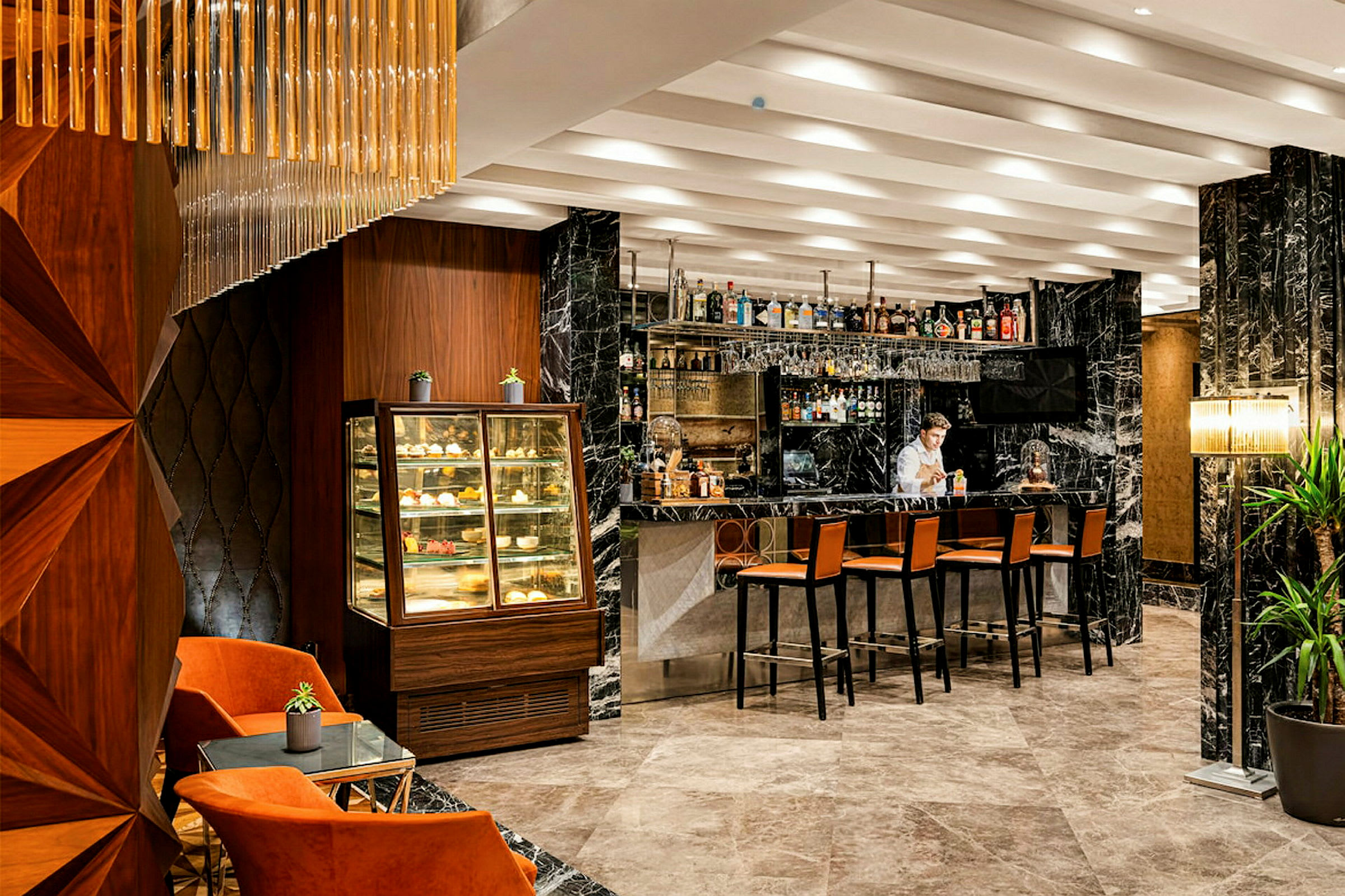 Interiøret i en elegant bar med marmordetaljer, en samling alkoholholdige drikker på hyllene, stoler ved baren og en utstillingsmonter for bakverk. (AI-generert tekst)