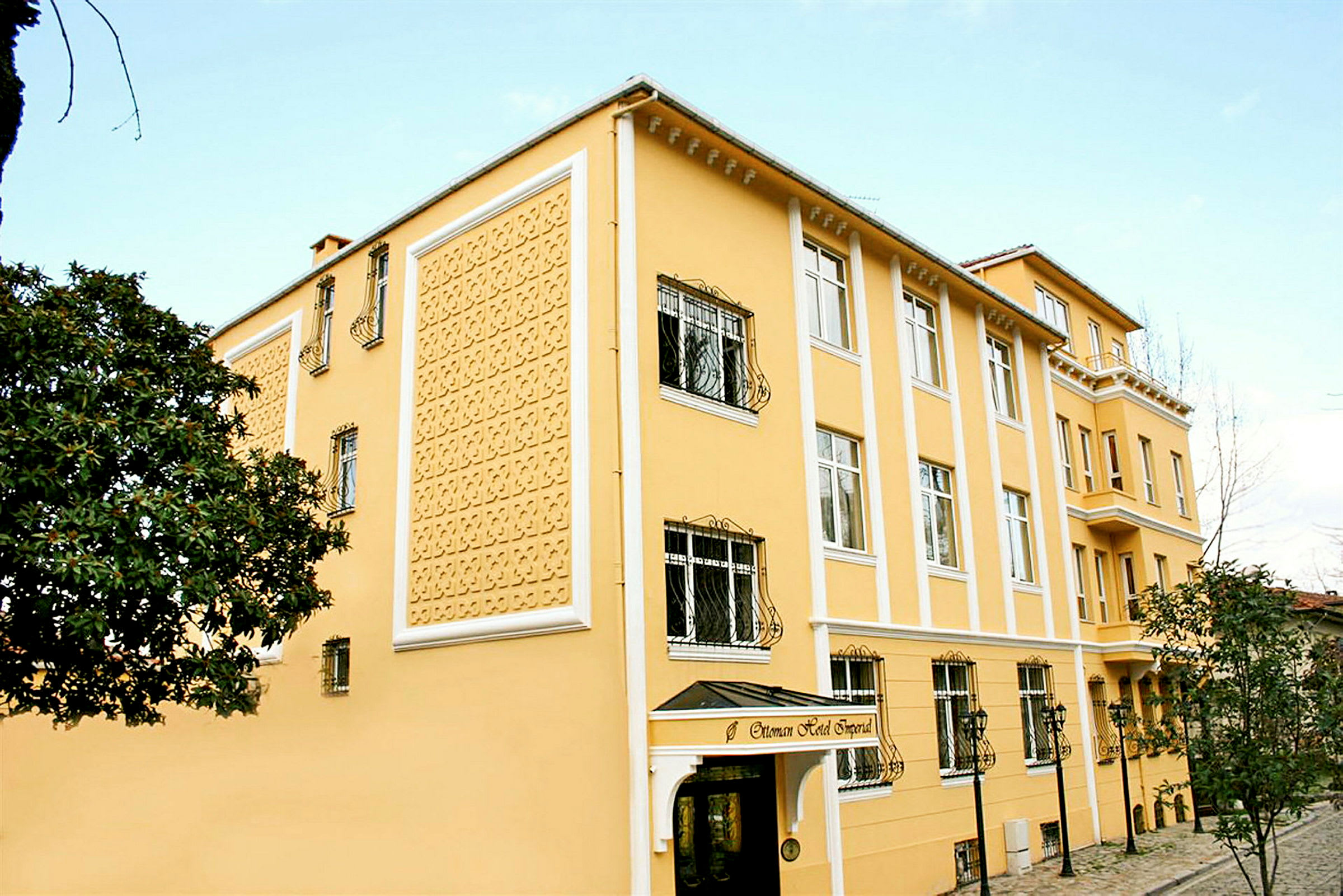 Et gult hotell med dekorativ fasade, vinduer med jernstenger og en inngang med takoverbygg. (AI-generert tekst)