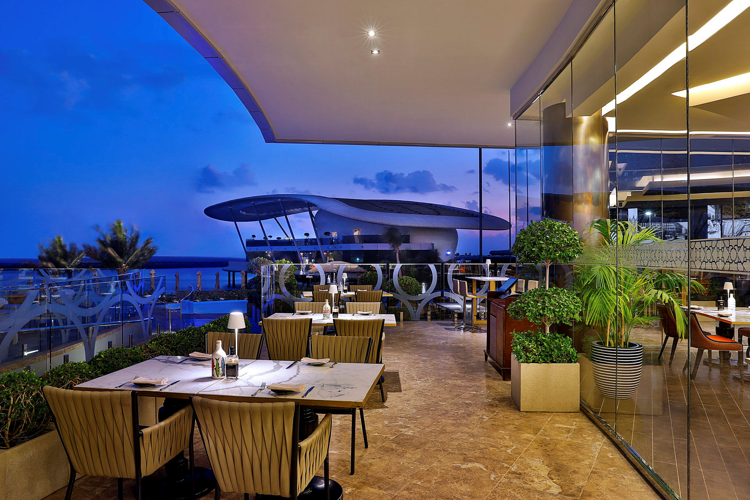 En restaurant med utsikt over havet og en futuristisk bygning i bakgrunnen. (AI-generert tekst)