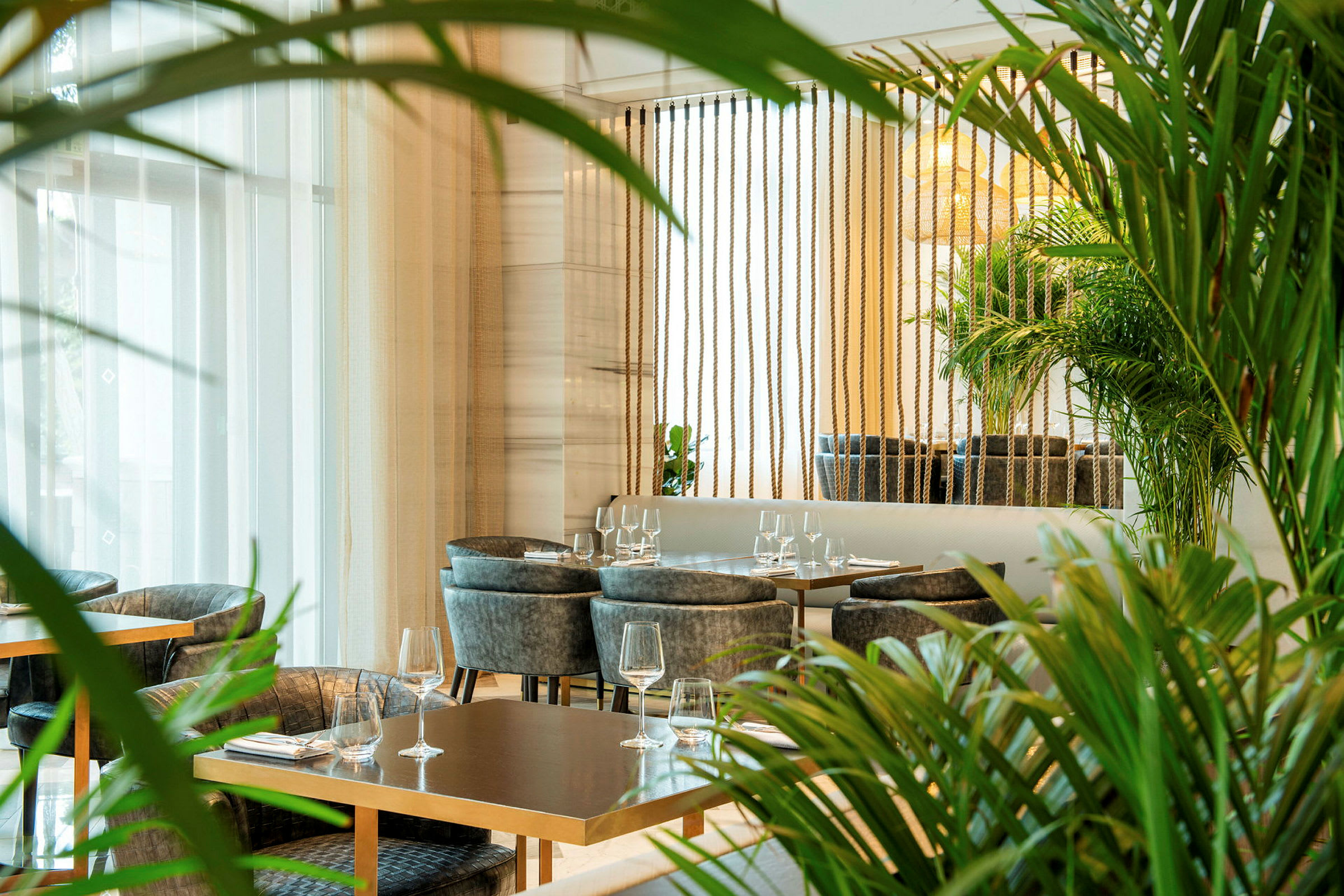 En moderne restaurant med bord og stoler omgitt av grønne planter. (AI-generert tekst)