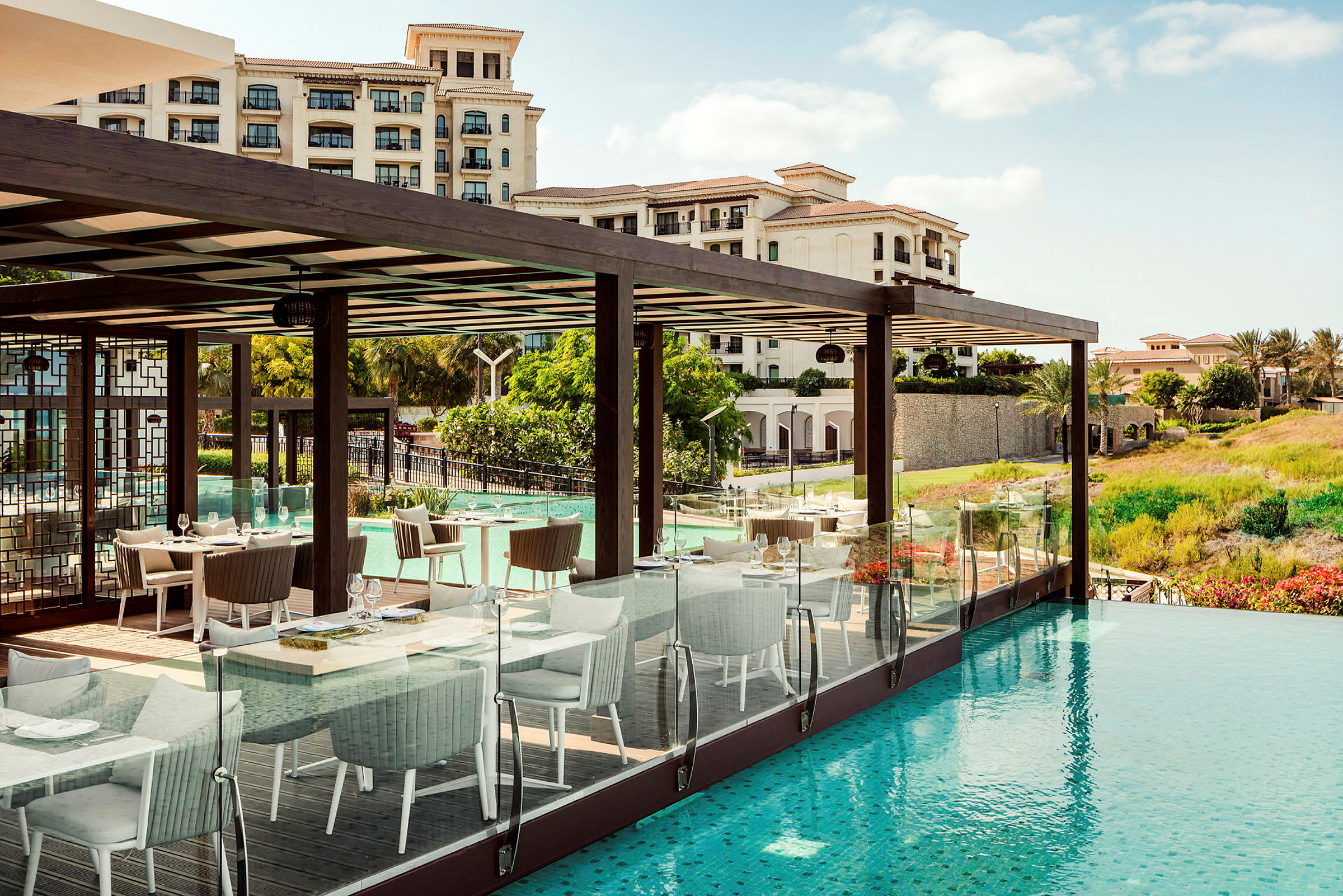 En utendørsrestaurant ved et basseng med hotellbygninger i bakgrunnen. (AI-generert tekst)