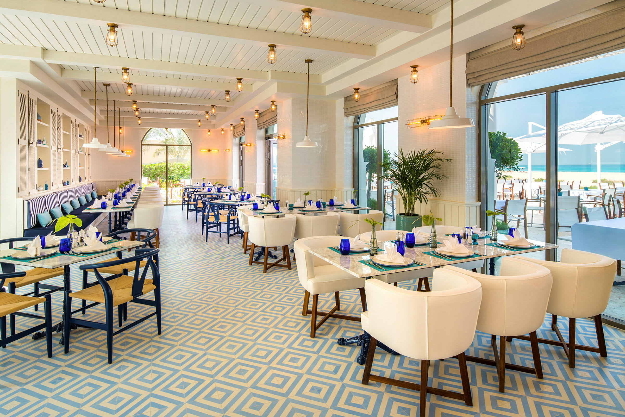 En elegant restaurant med store vinduer, blå og hvite fargetoner og utsikt mot havet. (AI-generert tekst)