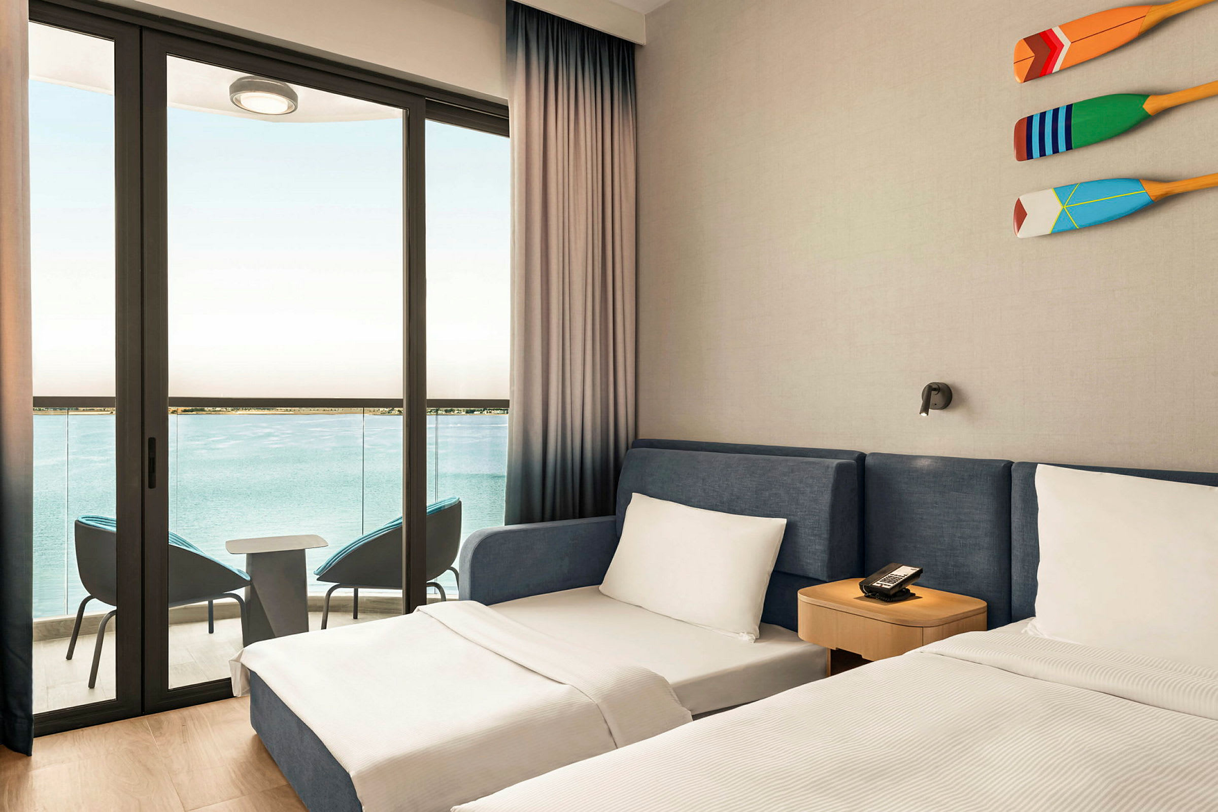Et hotellrom med to senger og en balkong med utsikt over havet. (AI-generert tekst)