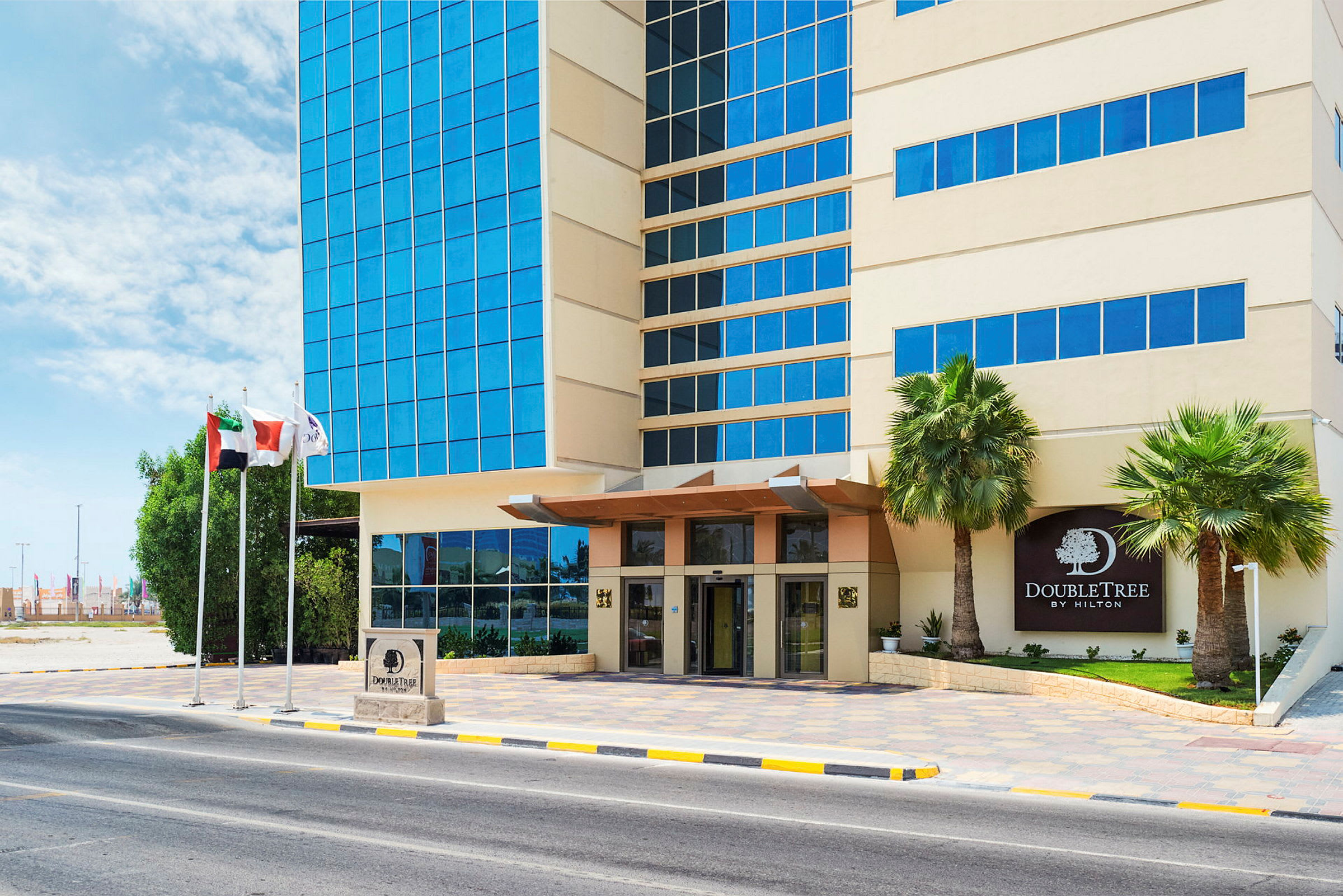 Eksteriør av DoubleTree Hotel med inngang, glassfasade og palmer ved siden av. (AI-generert tekst)