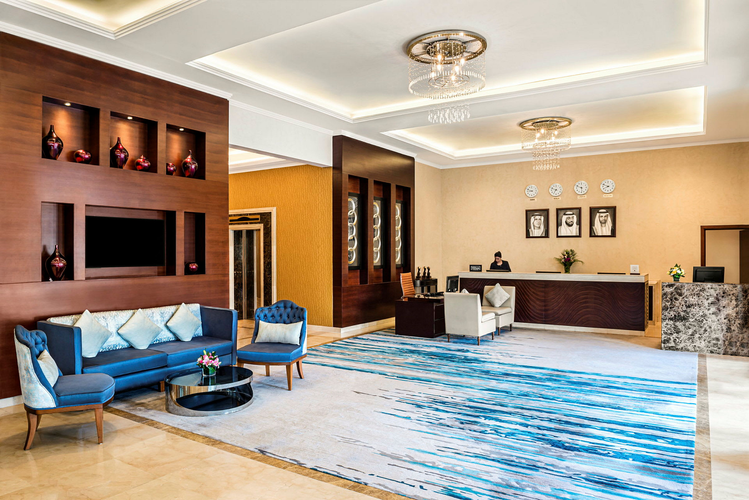 En elegant hotellobby med en sittegruppe med blå sofaer, et dekorativt resepsjonsområde og et marmorgulv. (AI-generert tekst)