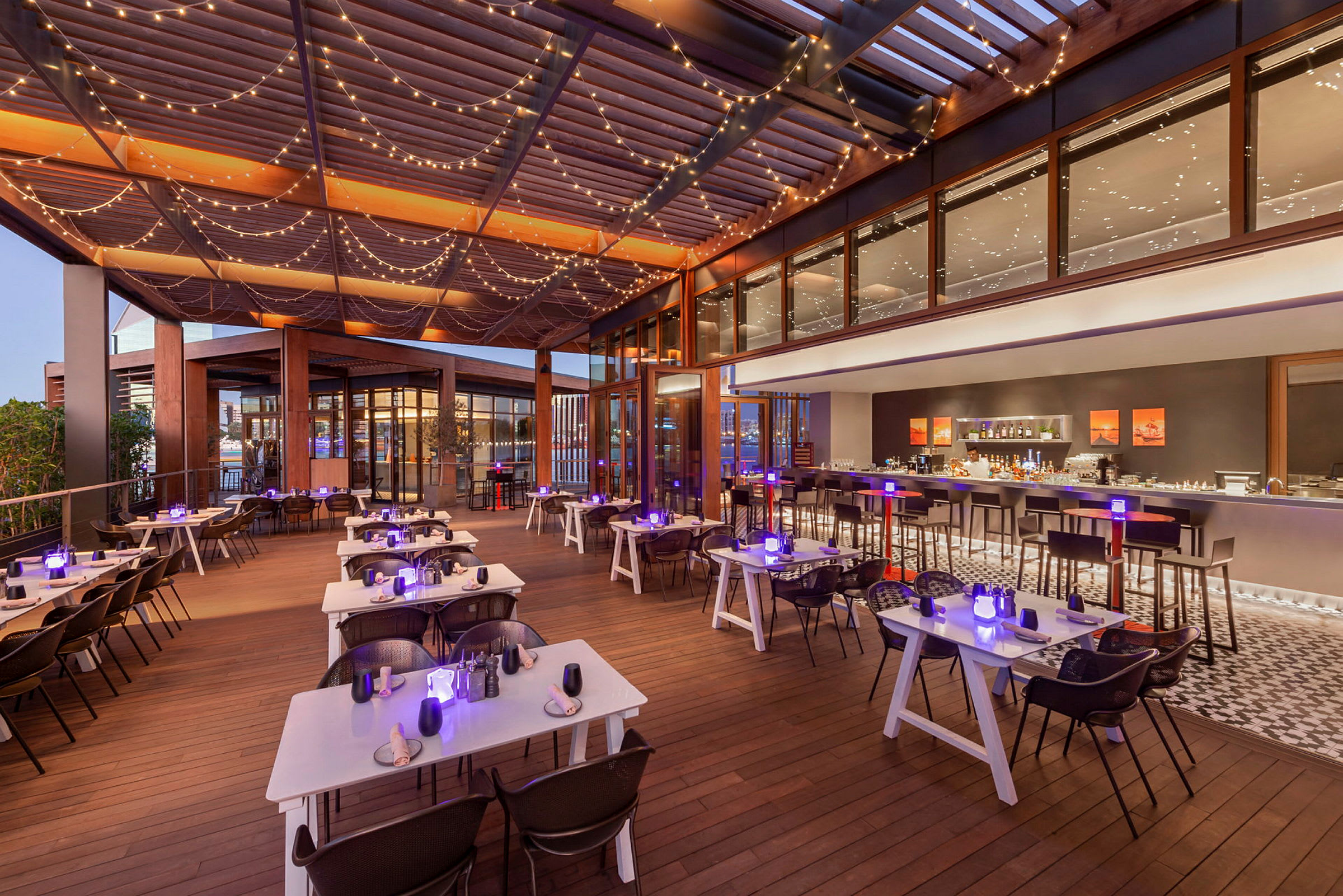 En restaurantterrasse med dekte bord og lysslynger i taket. (AI-generert tekst)