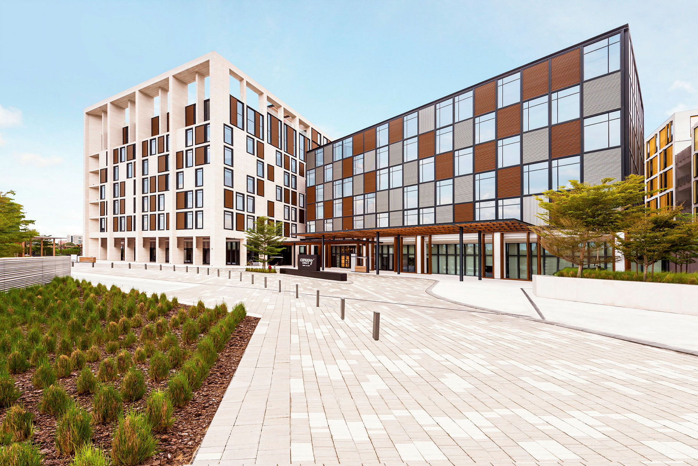 Et moderne hotell med en lys fasade og store vinduer, plassert ved et åpent torg. (AI-generert tekst)
