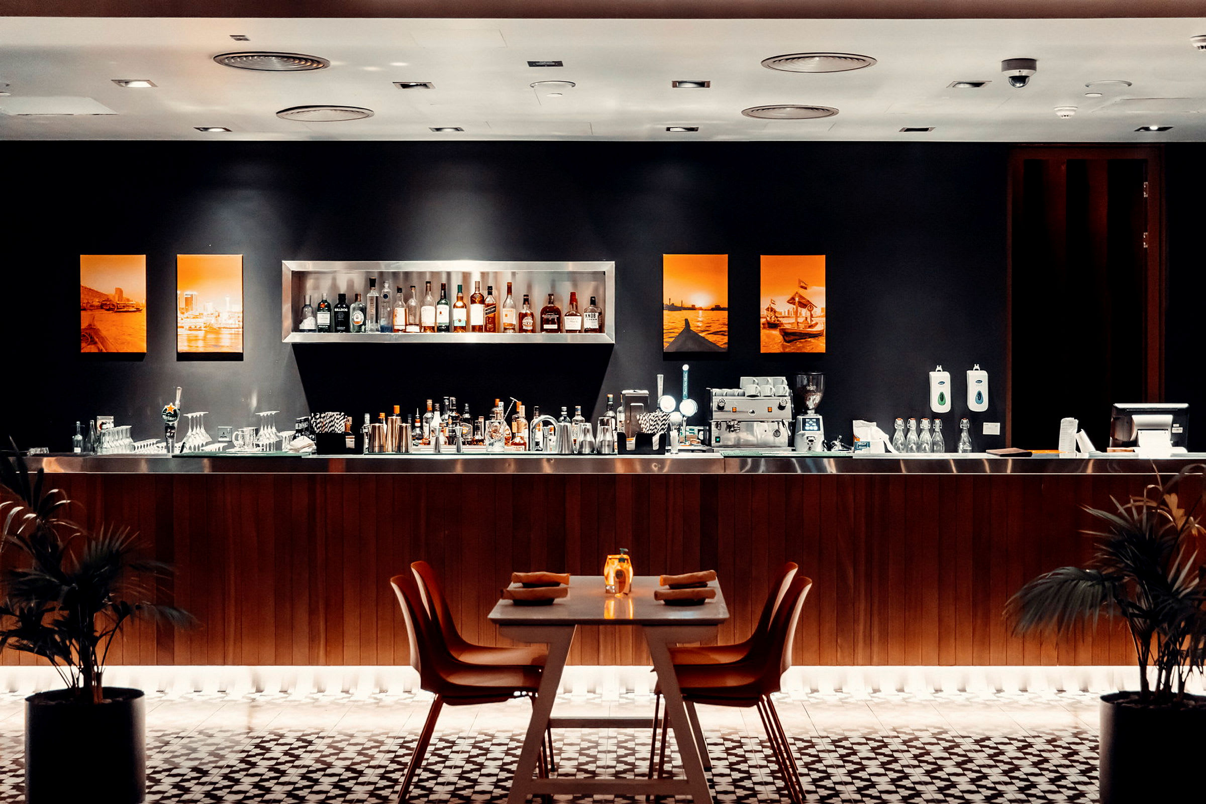 En elegant bar med hyller fylt med flasker, en benk med bartilbehør og et bord dekket for gjester i forgrunnen. (AI-generert tekst)