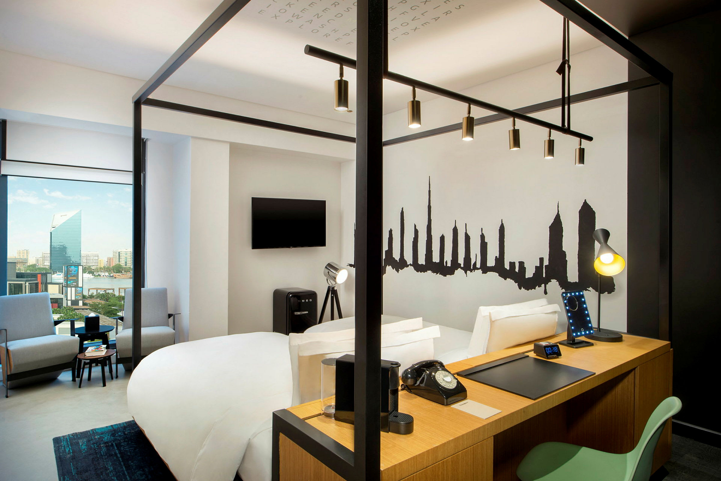 Et moderne hotellrom med en himmelseng, arbeidsbord, TV, sittegruppe og en bysilhuett malt på veggen. (AI-generert tekst)