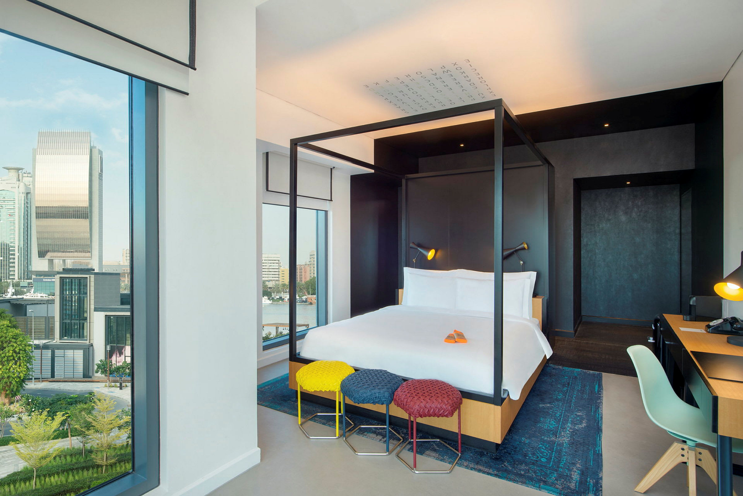 Moderne hotellrom med en himmelseng, skrivebord og store vinduer med utsikt over byen. (AI-generert tekst)