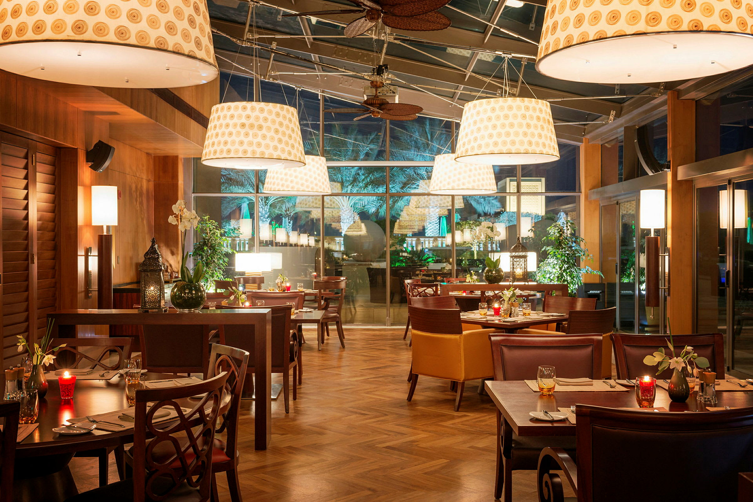 En restaurant med bord og stoler, belysning og en glassvegg. (AI-generert tekst)