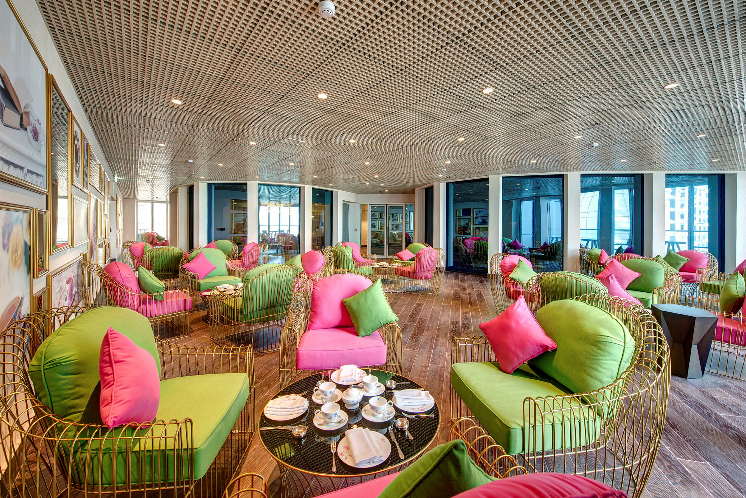 Et innemiljø med moderne sittemøbler i sterke farger, inkludert grønne og rosa puter, samt glassbord med servering. (AI-generert tekst)