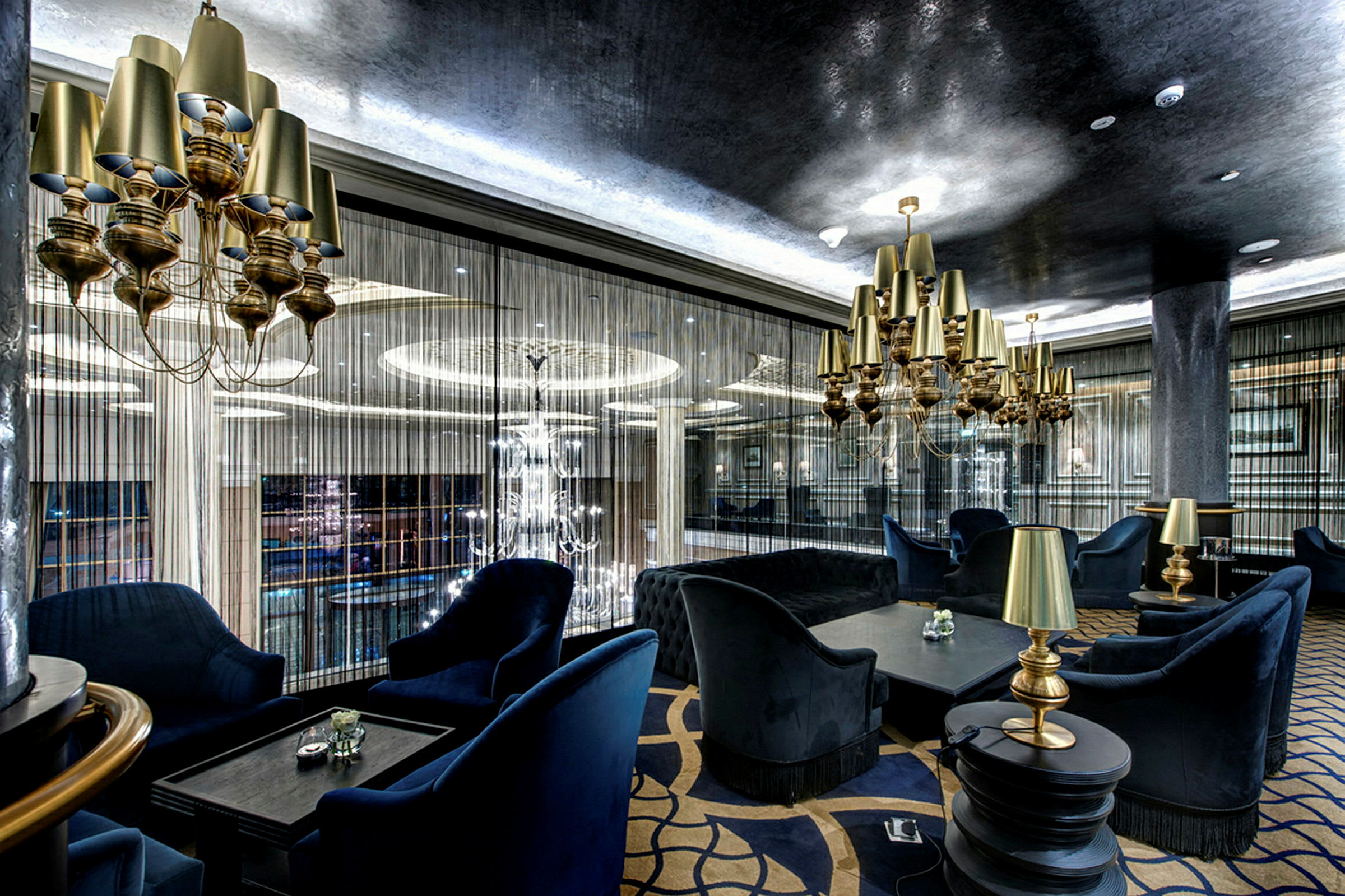 En elegant lounge med blå polstrede møbler, gullamper og moderne hengende lysekroner. (AI-generert tekst)