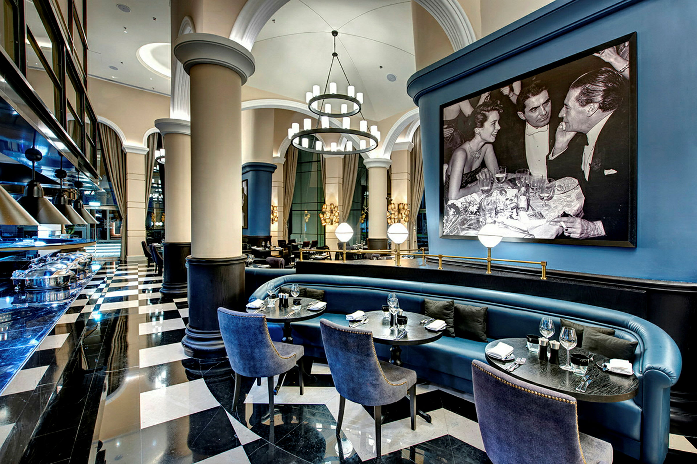 Interiør av en elegant restaurant med svart-hvitt gulv, blå sitteplasser og et stort innrammet svart-hvitt bilde. (AI-generert tekst)